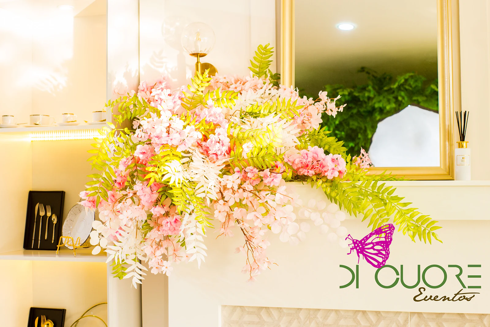 Arranjo de flores cor-de-rosa e brancas com folhagem verde sobre uma lareira, junto a um espelho de moldura dourada