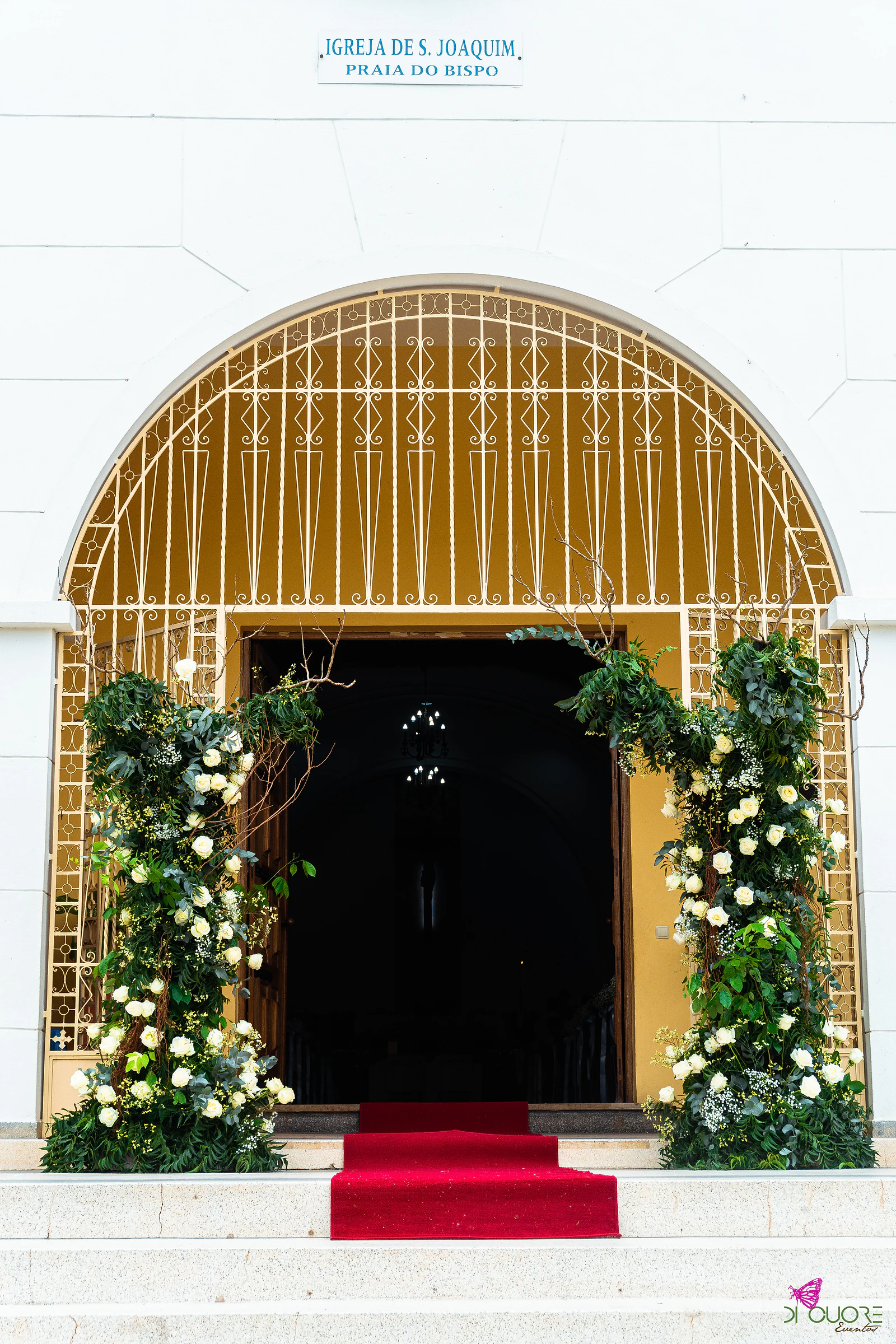 Portal em arco da igreja com duas colunas de rosas brancas e folhagem e tapete vermelho à entrada