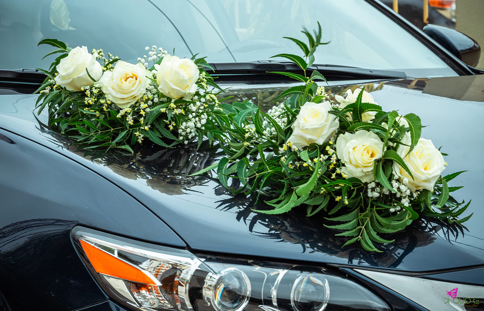 Grinalda de rosas brancas, gipsófila e folhagem sobre o capô de um carro escuro
