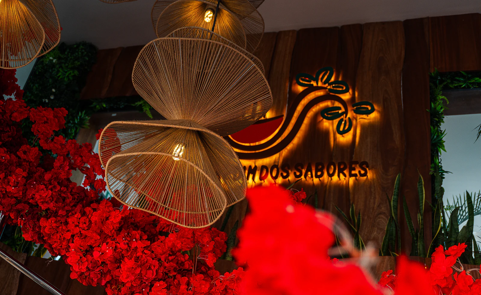 Letreiro luminoso do restaurante entre candeeiros de vime e flores vermelhas