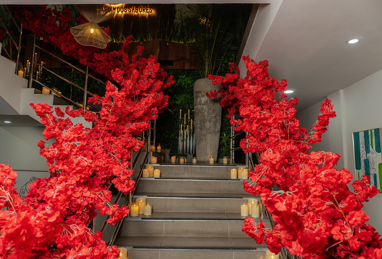 Escadaria ladeada por ramos de flores vermelhas, com velas nos degraus