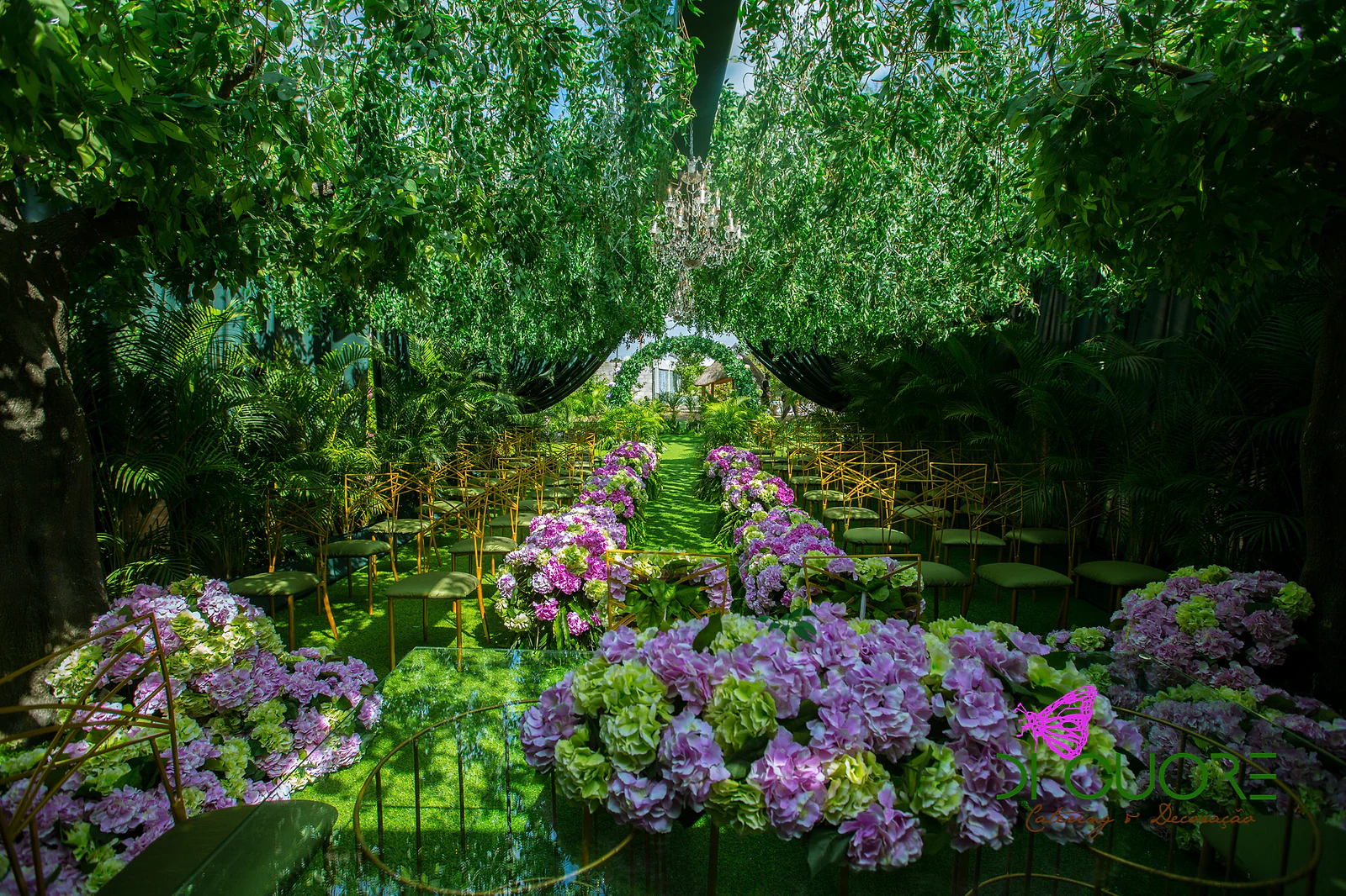 Civil ceremony in a forest-like garden, with foliage covering the ceiling, a crystal chandelier, rows of gold chairs and large arrangements of purple hydrangeas