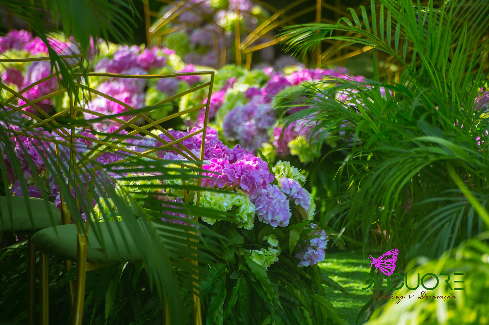 Lilac and lime-green hydrangeas among palms and a gold chair, in garden light