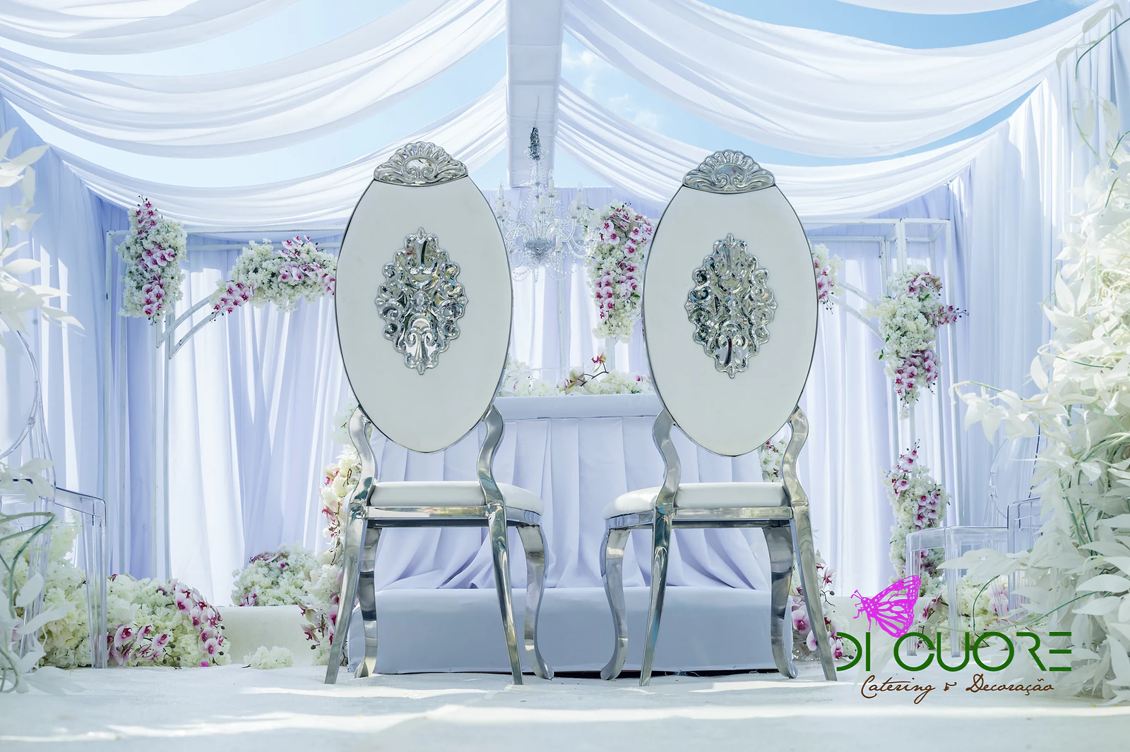 Two tall chairs with oval silver backs between white drapes and small sprays of orchids