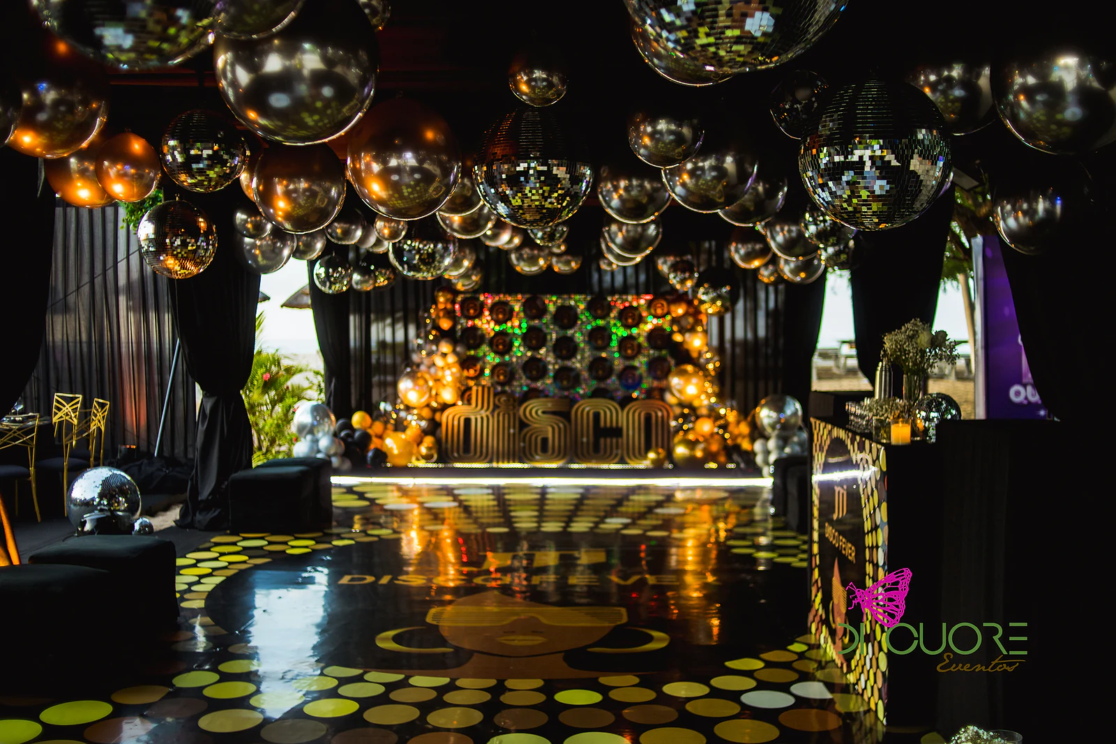 Pista de pontos dourados sob um tecto de esferas prateadas e douradas, com o palco DISCO ao fundo