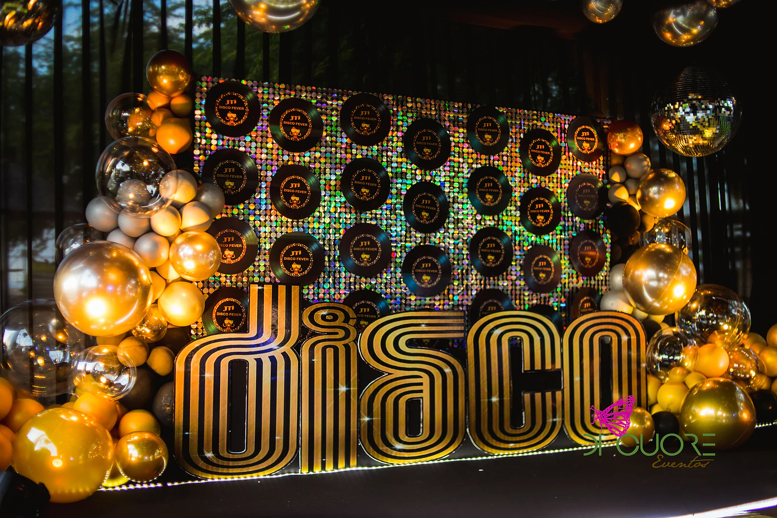 Letras douradas DISCO diante de um painel holográfico com discos de vinil, entre aglomerados de balões dourados e prateados
