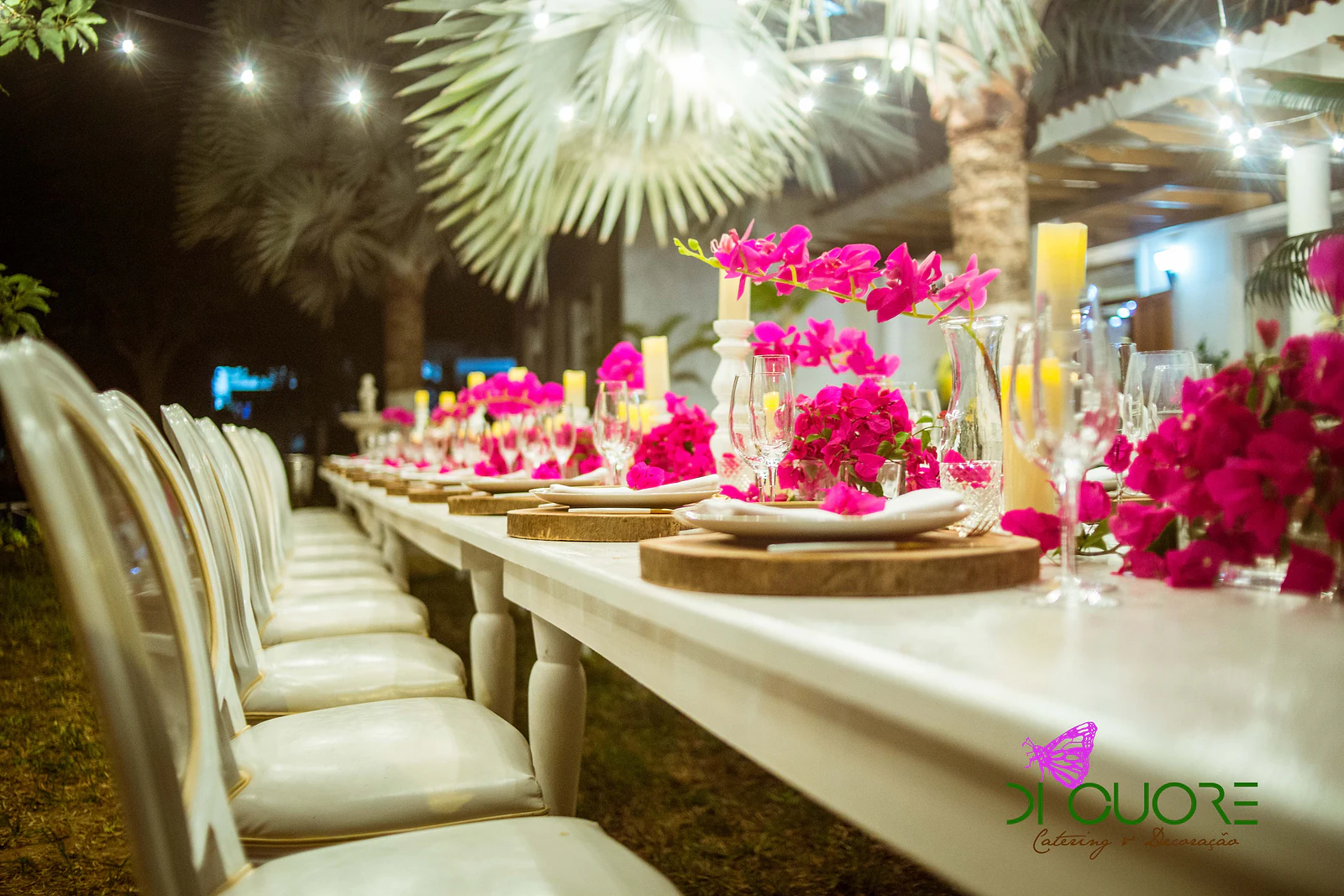 White candlestick with a yellow candle and a bougainvillea spray at the centre of the table, between plates on wooden slices