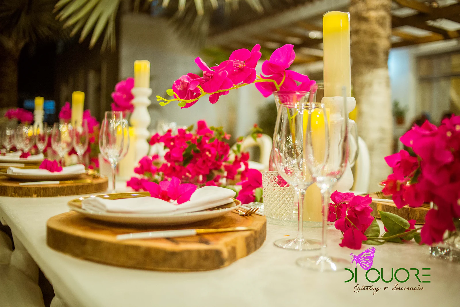 Laid table with a plate on a wooden slice, white candlesticks with yellow candles and sprays of fuchsia flowers