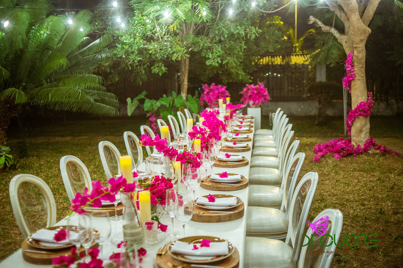 Laid table with yellow candles, bougainvillea sprays and white chairs, with the flowered trunk on the right