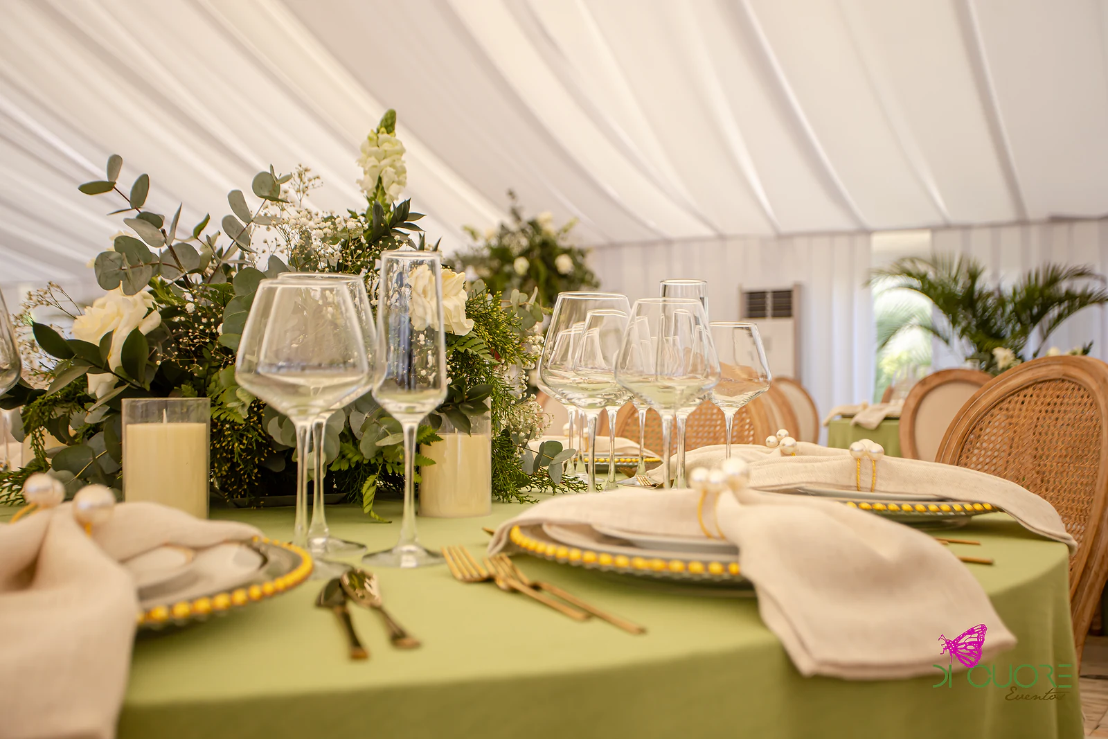Pormenor de mesa com copos de cristal, velas de coluna, ramo de eucalipto e rosas brancas e guardanapos de linho com argola de pérola