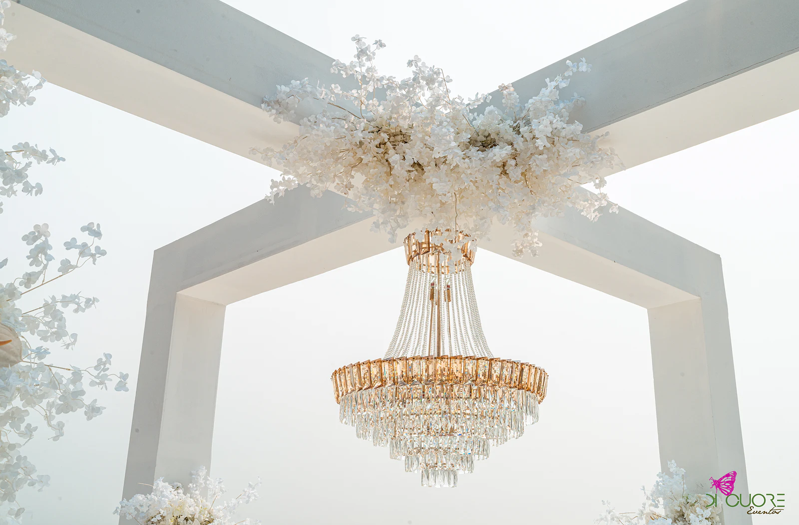 O arco branco visto de baixo, com a coroa de flores brancas e o lustre de cristal dourado suspenso no centro