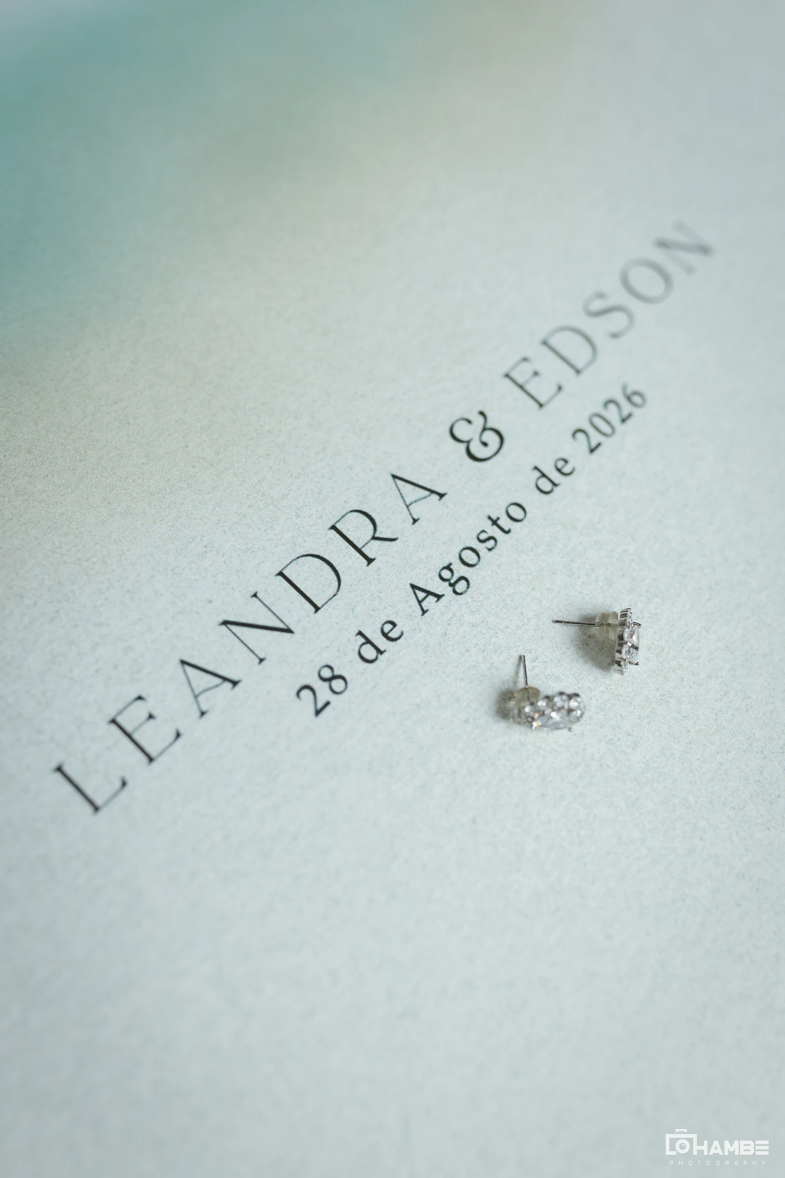 Cartão com os nomes Leandra & Edson e a data, 28 de agosto de 2026, junto a um par de brincos de cristais