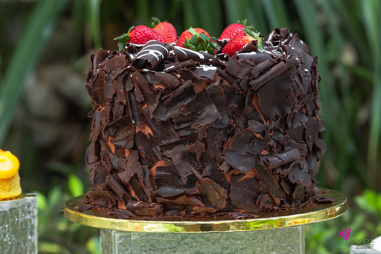 Bolo de chocolate coberto de lascas de chocolate e morangos, sobre uma base dourada