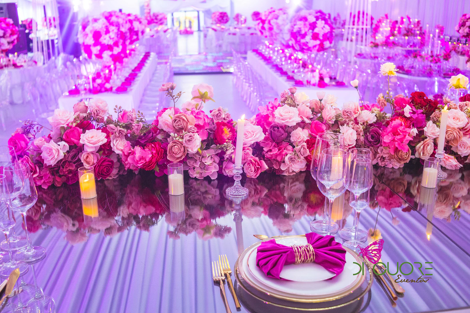 Mesa de espelho com um friso de rosas cor-de-rosa e vermelhas, velas e um prato com guardanapo fúcsia em laço