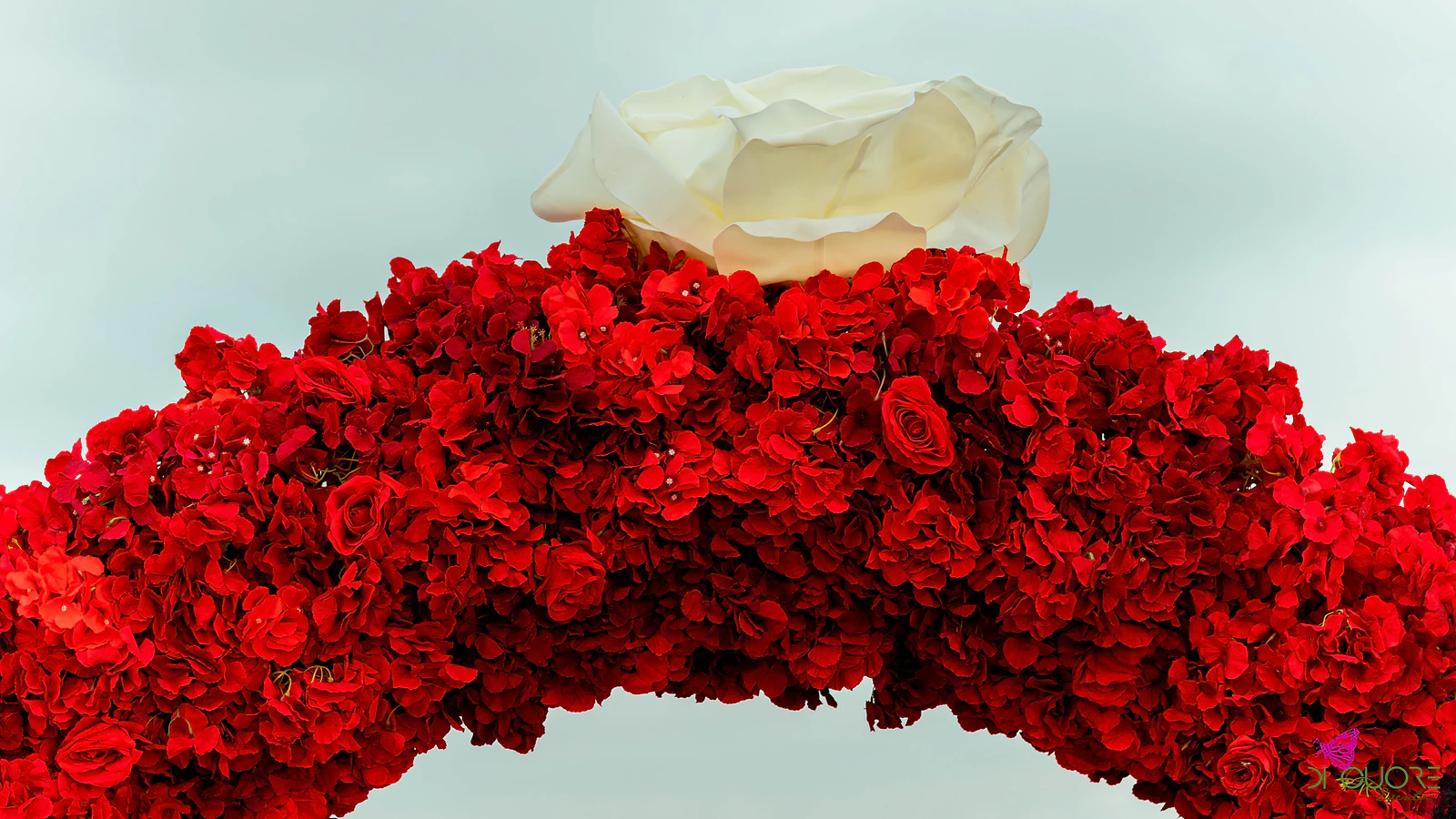 Pormenor do topo do arco: uma rosa branca gigante sobre um maciço de rosas e flores vermelhas