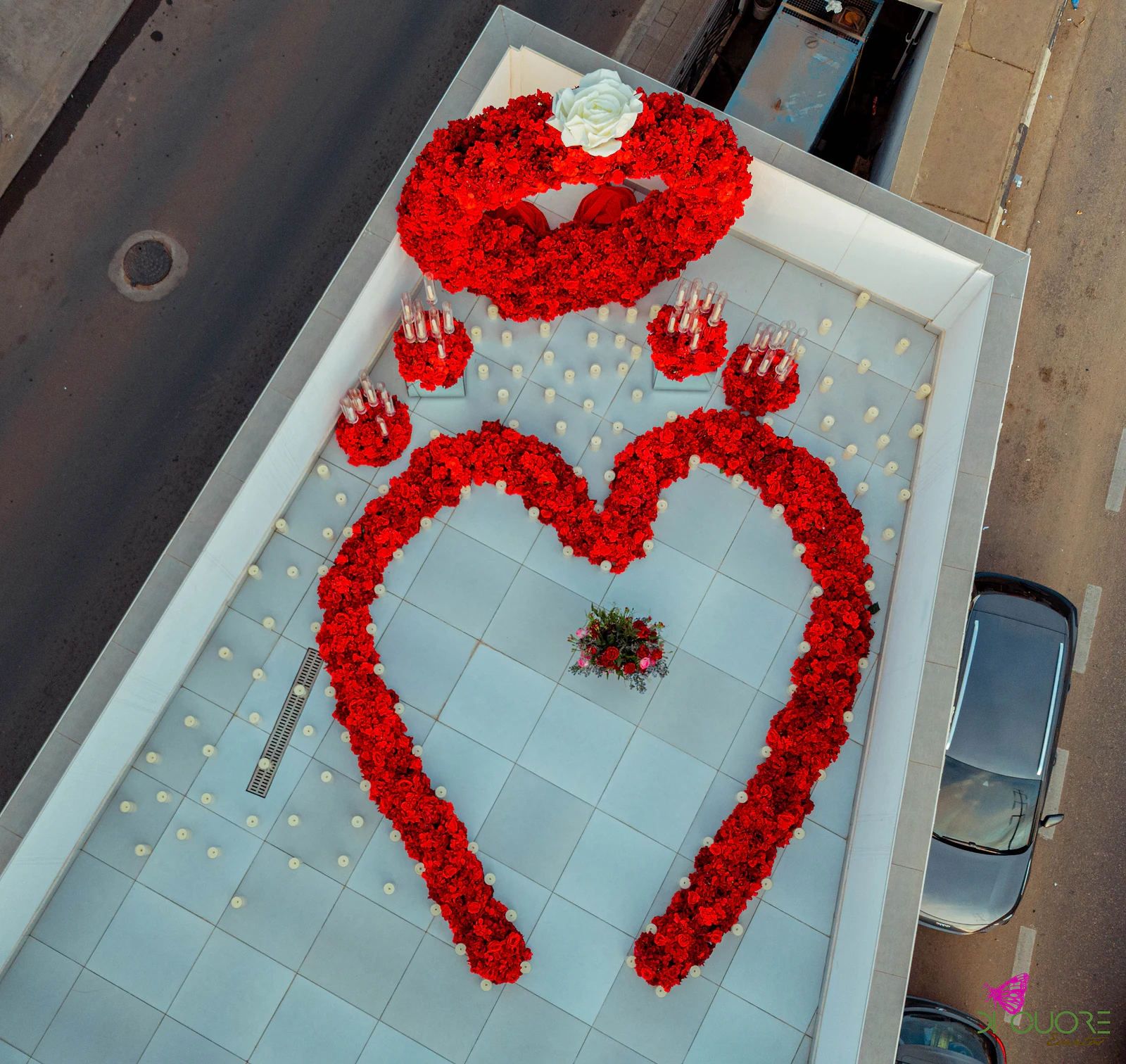 Vista aérea de dia do coração de rosas vermelhas desenhado no piso do terraço, com o arco em cima e o ramo ao centro