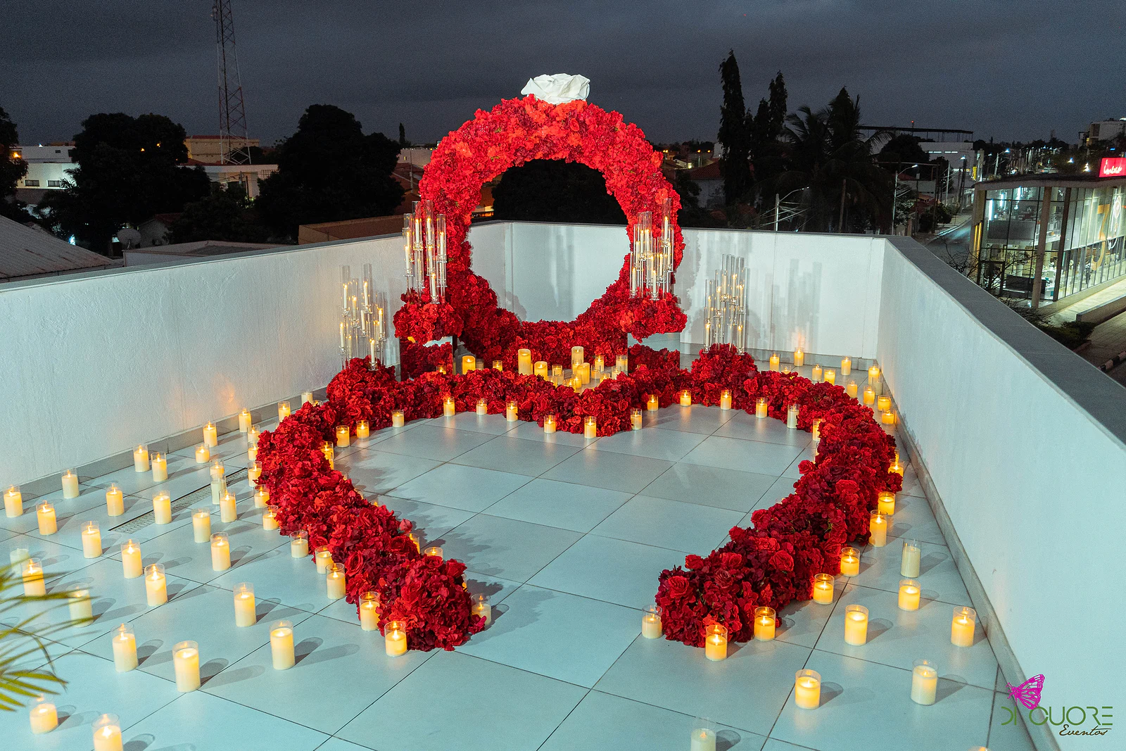 Terraço ao anoitecer com o arco de rosas vermelhas rematado por uma rosa branca e um coração de rosas rodeado de velas