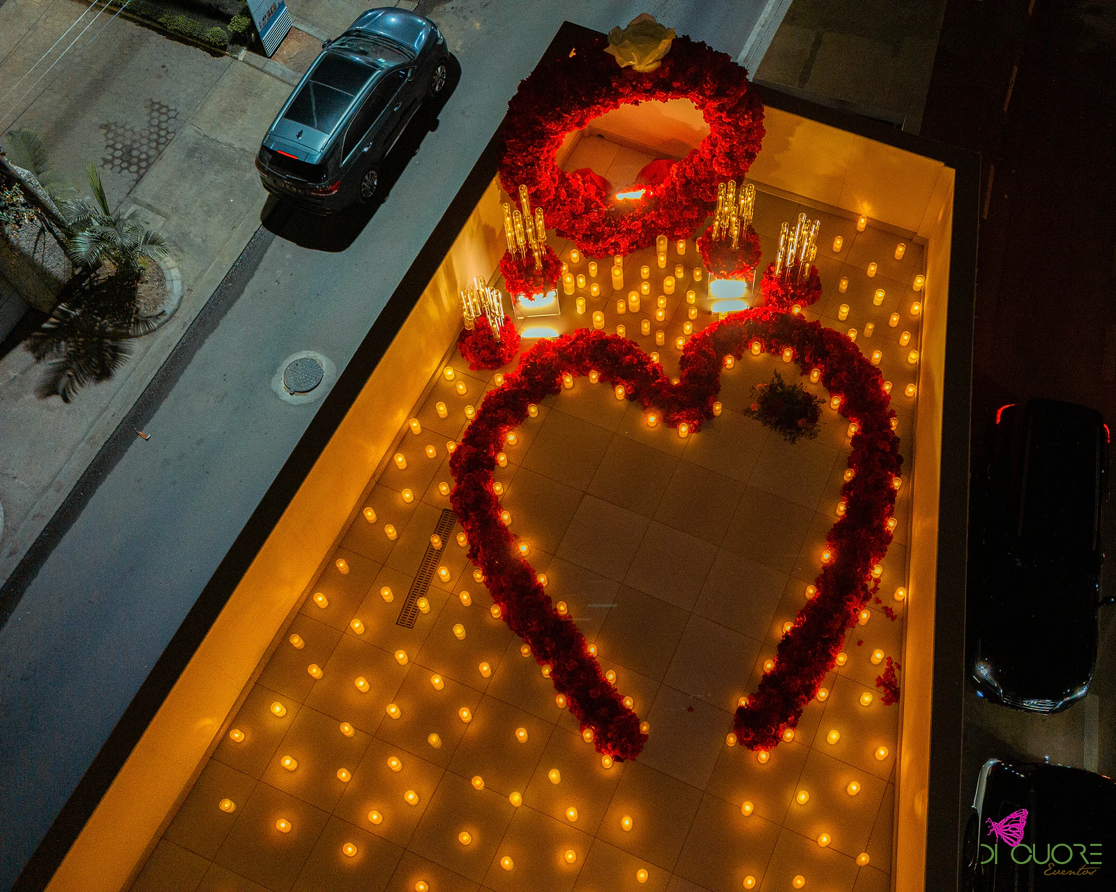 Vista aérea ao anoitecer de um terraço com um coração de rosas vermelhas e velas acesas, iluminado em tons âmbar