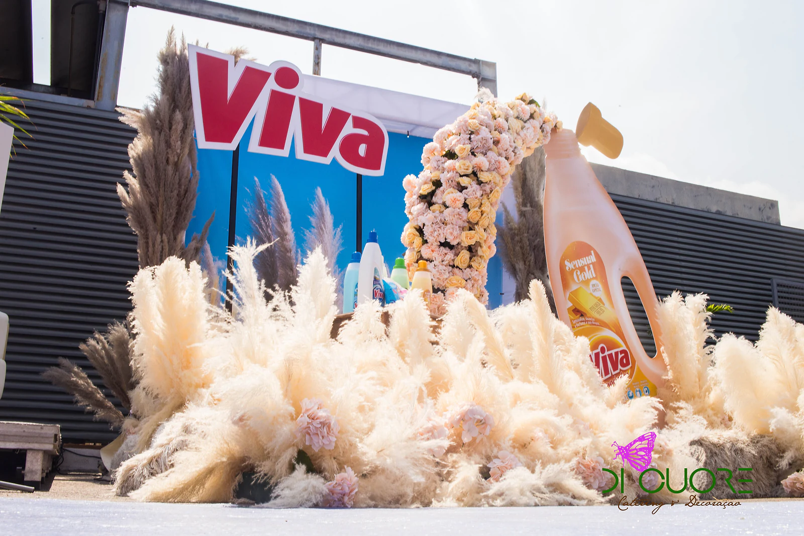 Mar de plumas de erva-das-pampas cor de creme diante de um arco de rosas que se derrama de um frasco Viva gigante