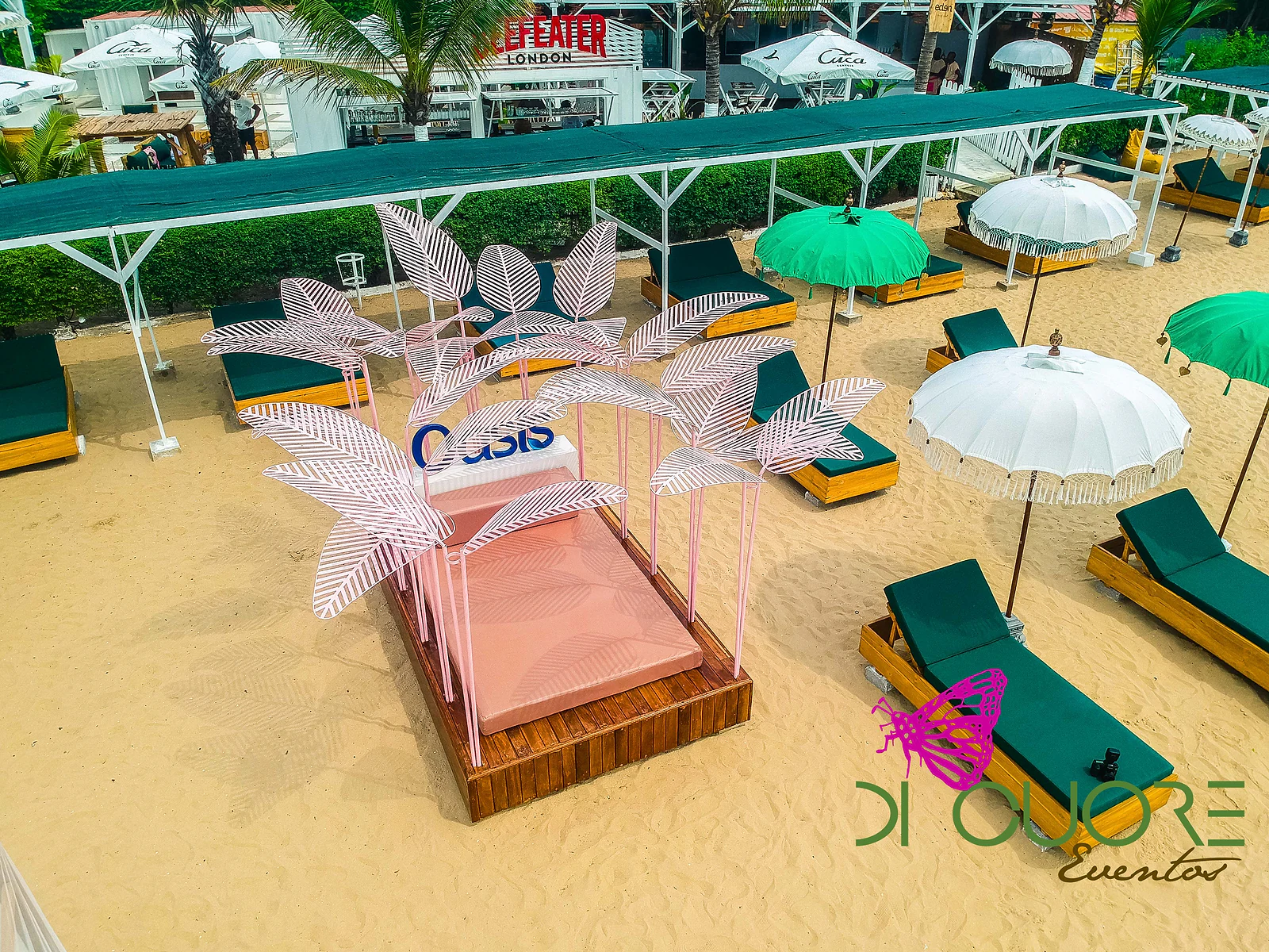Vista aérea da cama de deck com folhas cor-de-rosa na praia, entre espreguiçadeiras verdes e guarda-sóis