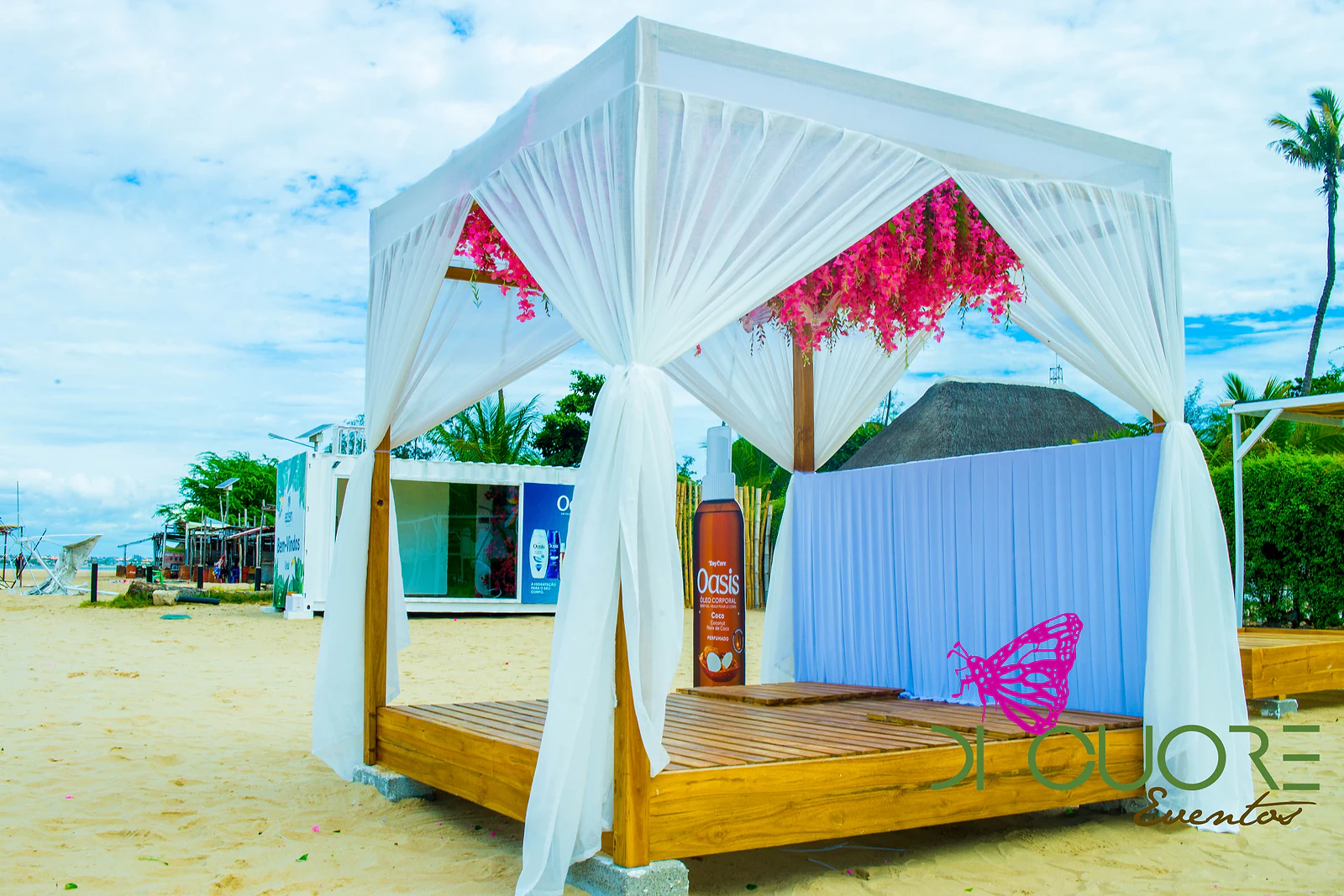 Cabana de madeira com cortinados brancos, flores cor-de-rosa suspensas e painel pregueado azul-claro, na praia