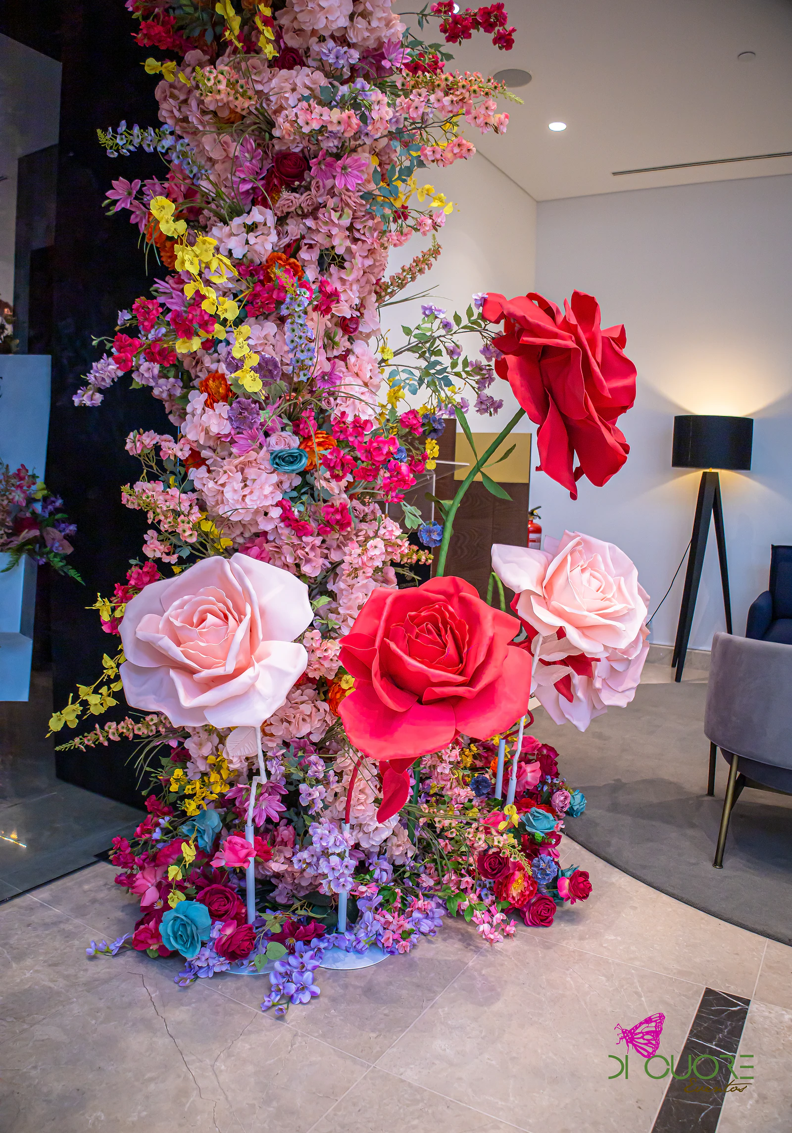 Coluna de flores cor-de-rosa, vermelhas e amarelas com rosas gigantes vermelhas e cor-de-rosa, num átrio de pavimento claro