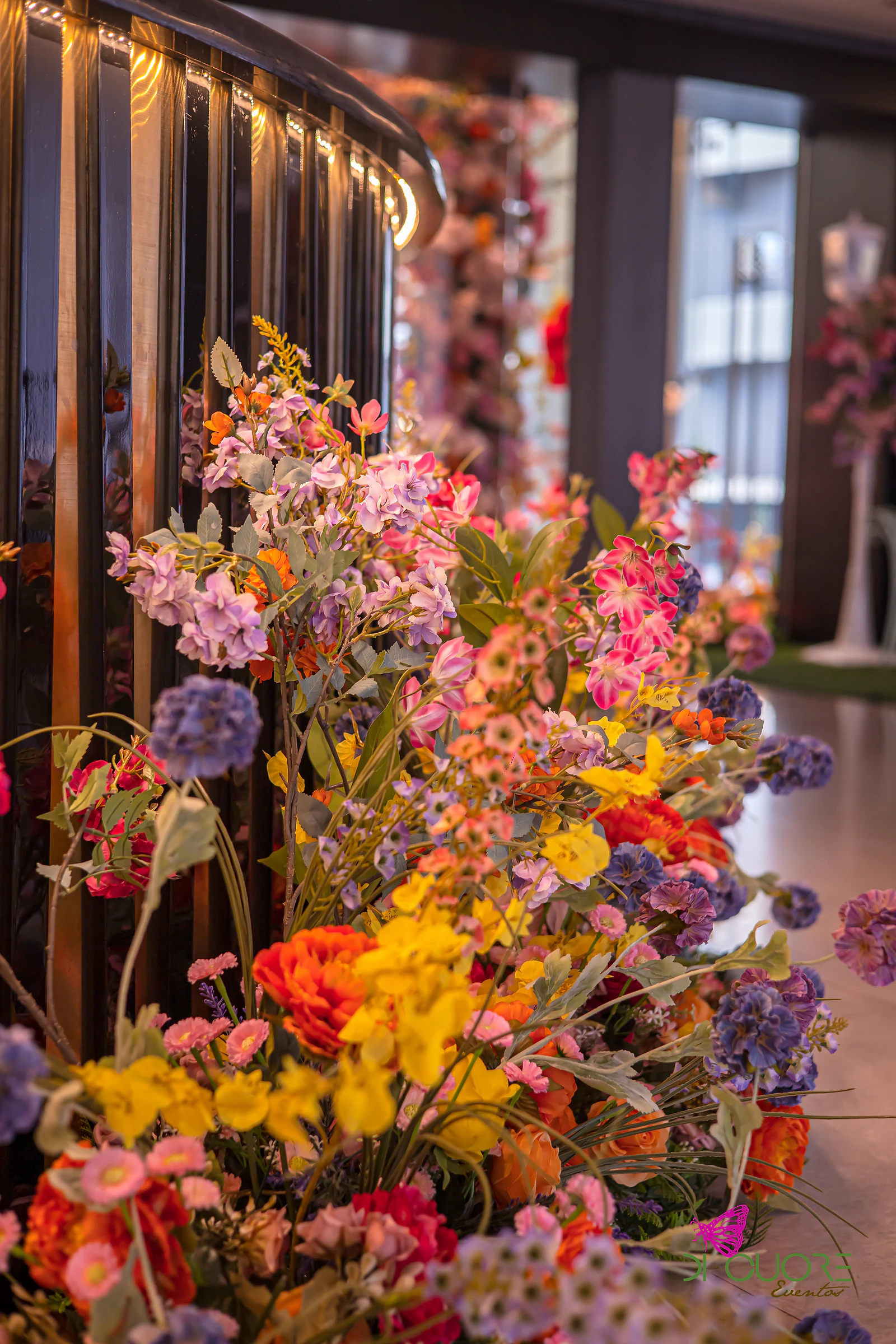 Sprays of yellow, orange, purple and pink flowers beside a black railing with a strip of light