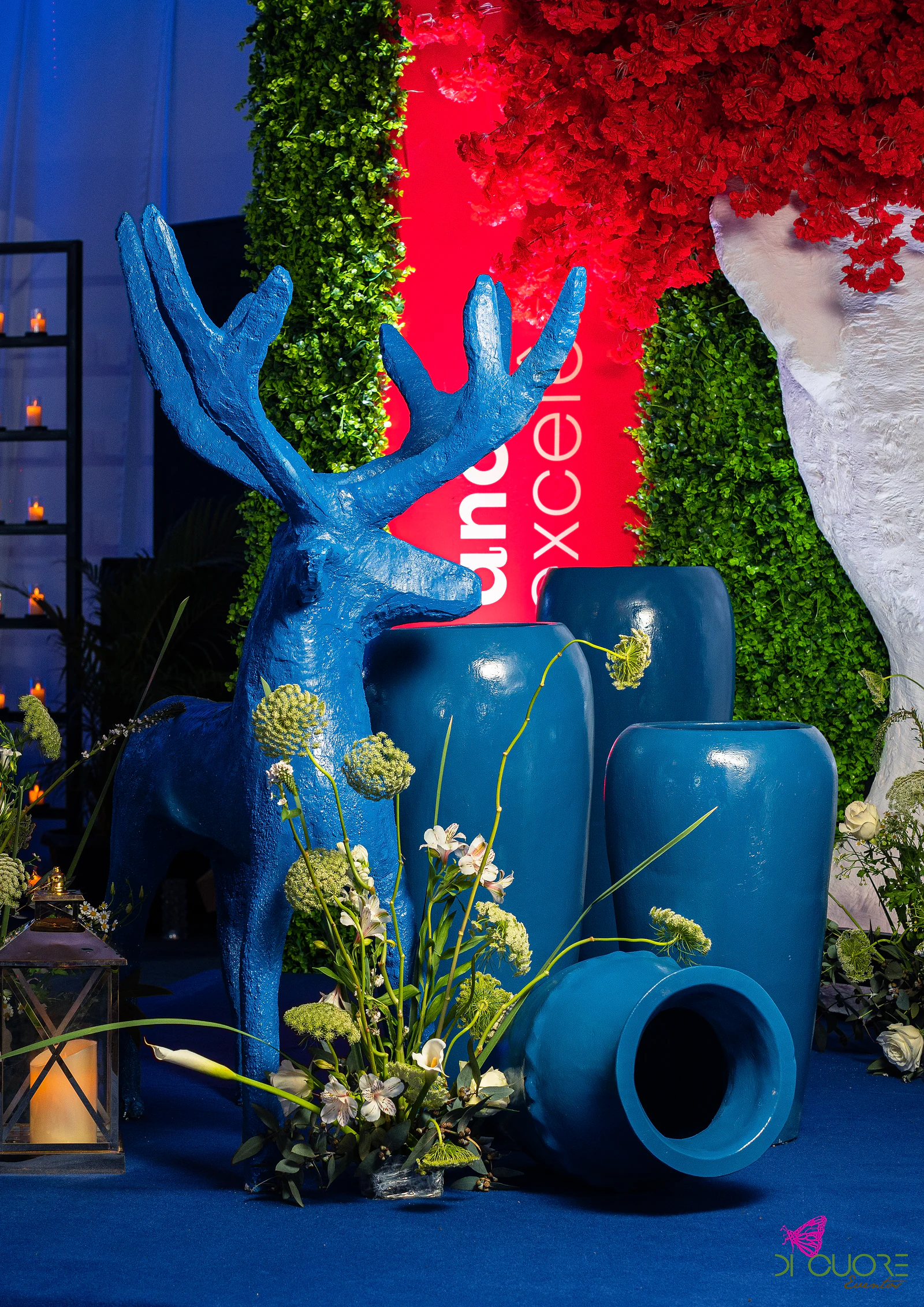 Veado azul e jarros altos em azul-cobalto com flores brancas e verdes, uma lanterna acesa e um painel vermelho ao fundo