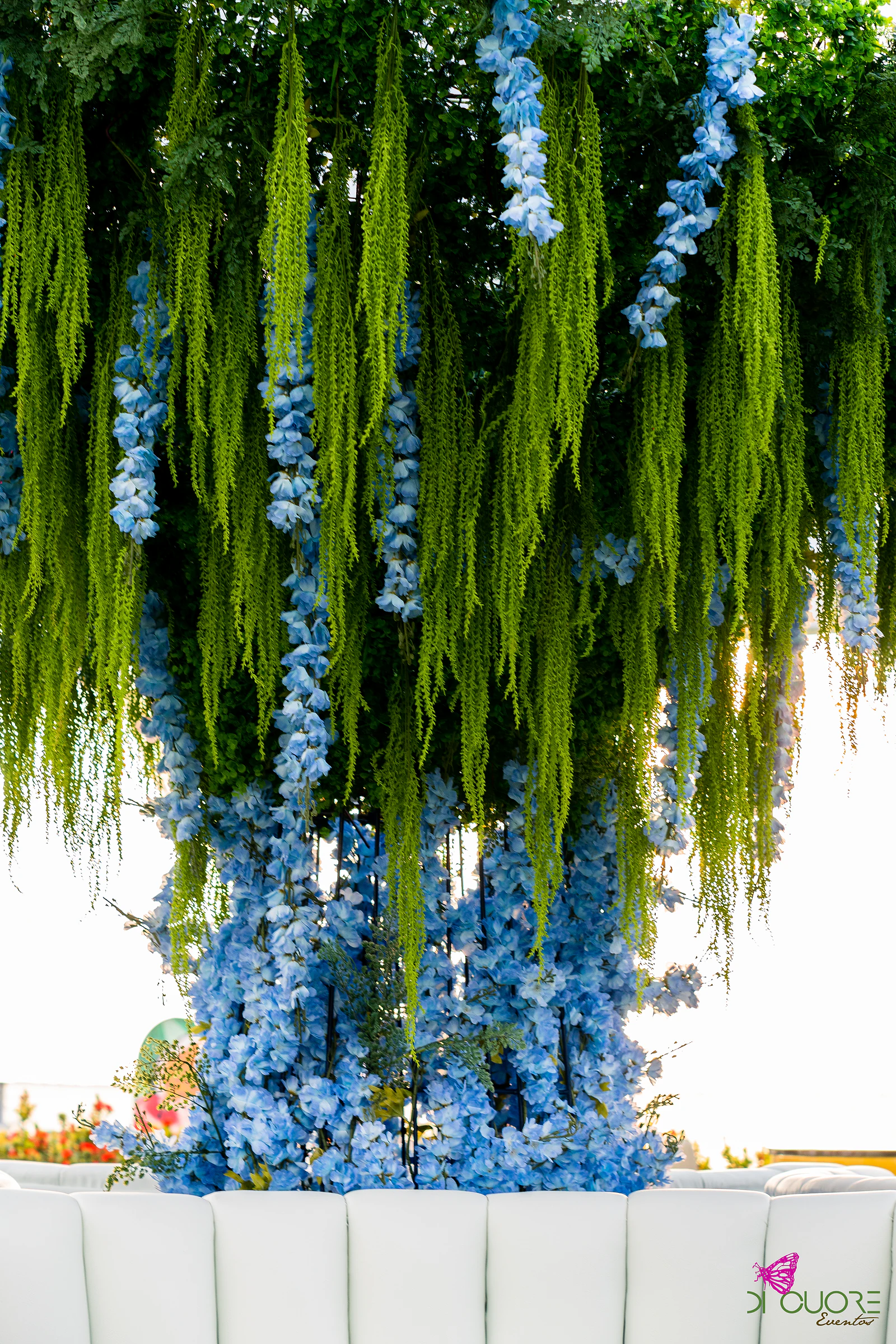 Cascata de flores azuis e amaranto verde suspensa, com o espaldar de um sofá branco em baixo