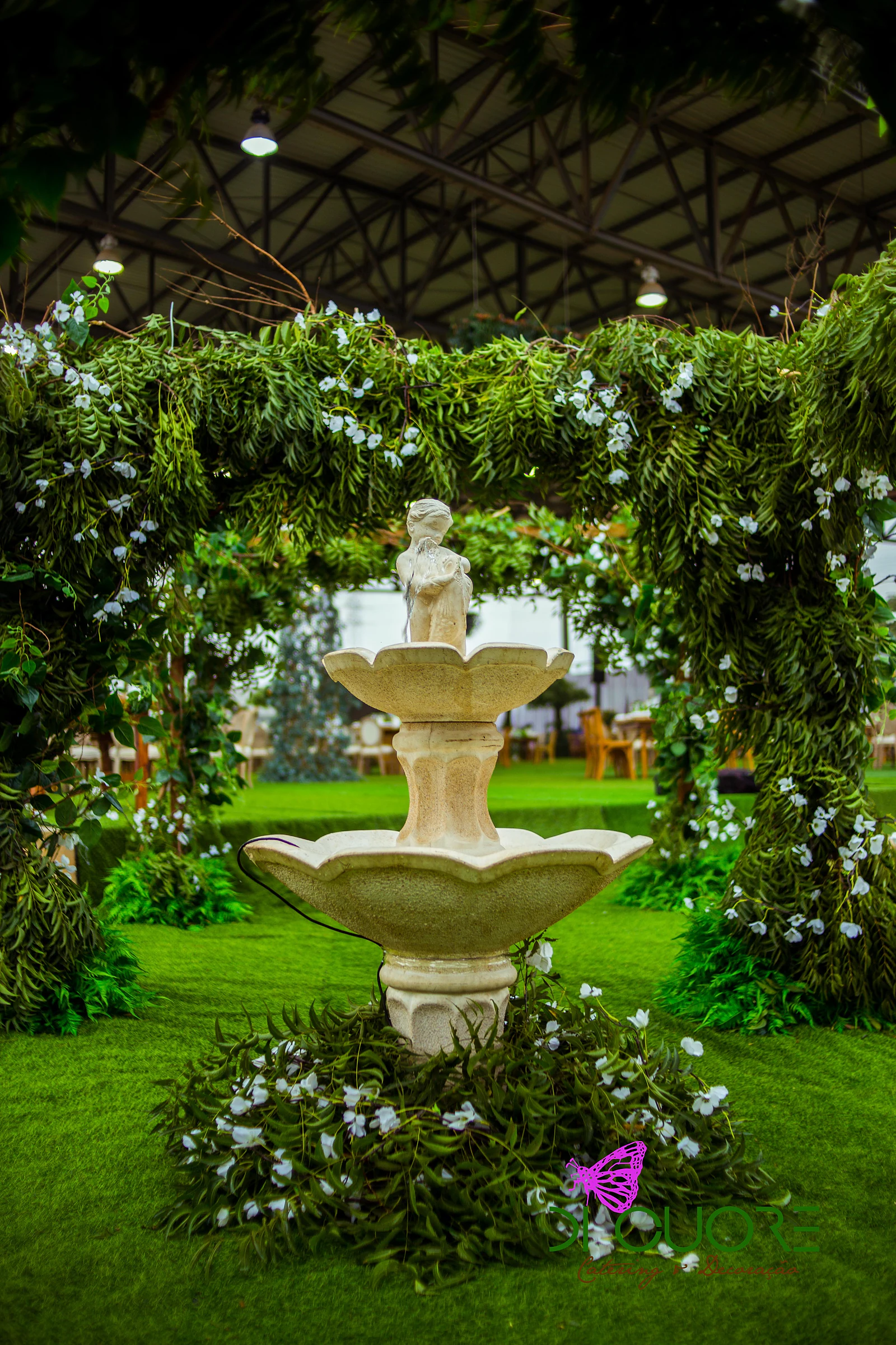 Fonte de pedra clara sob um arco de folhagem e pequenas flores brancas, sobre relva