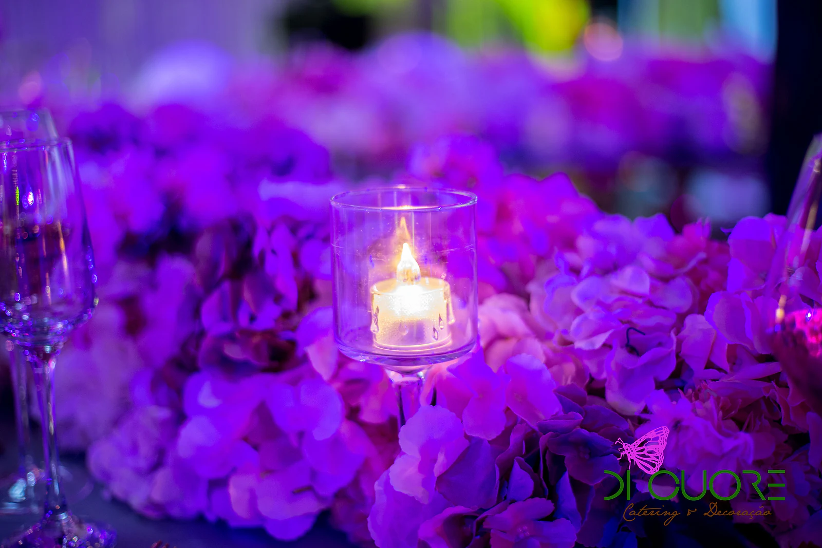 Vela num copo de vidro rodeada de hortênsias lilases e fúcsia