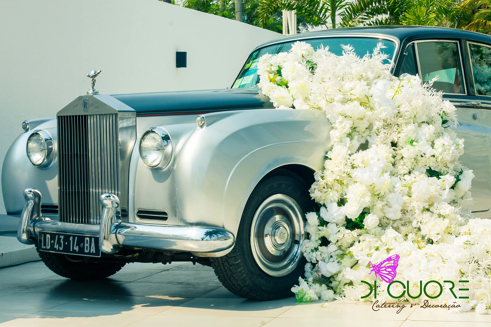 Carro clássico prateado e verde-escuro com uma cascata de flores brancas a descer do capô até ao chão