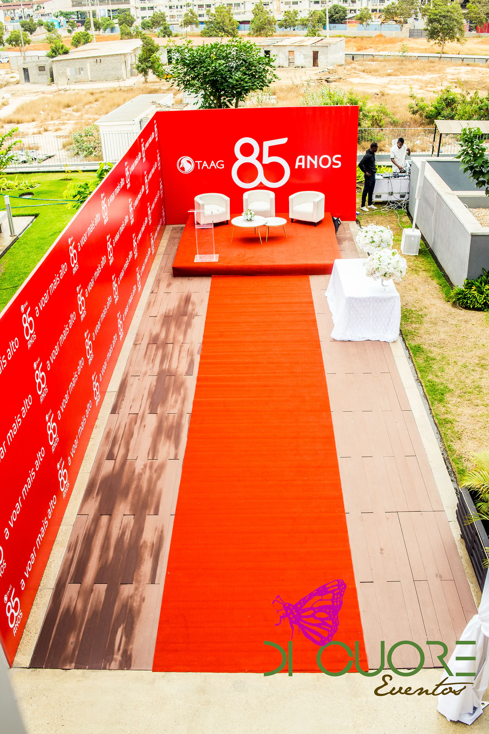 Vista de cima do palco vermelho com o logótipo TAAG e o 85 anos, poltronas brancas, púlpito transparente e uma passadeira vermelha ao centro do deque