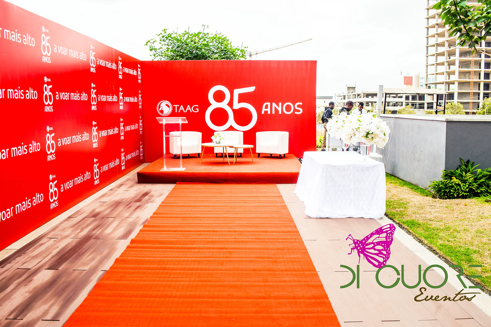 Passadeira vermelha a conduzir ao palco com o 85 anos, entre os painéis do lema “a voar mais alto” e uma mesa de toalha branca com flores