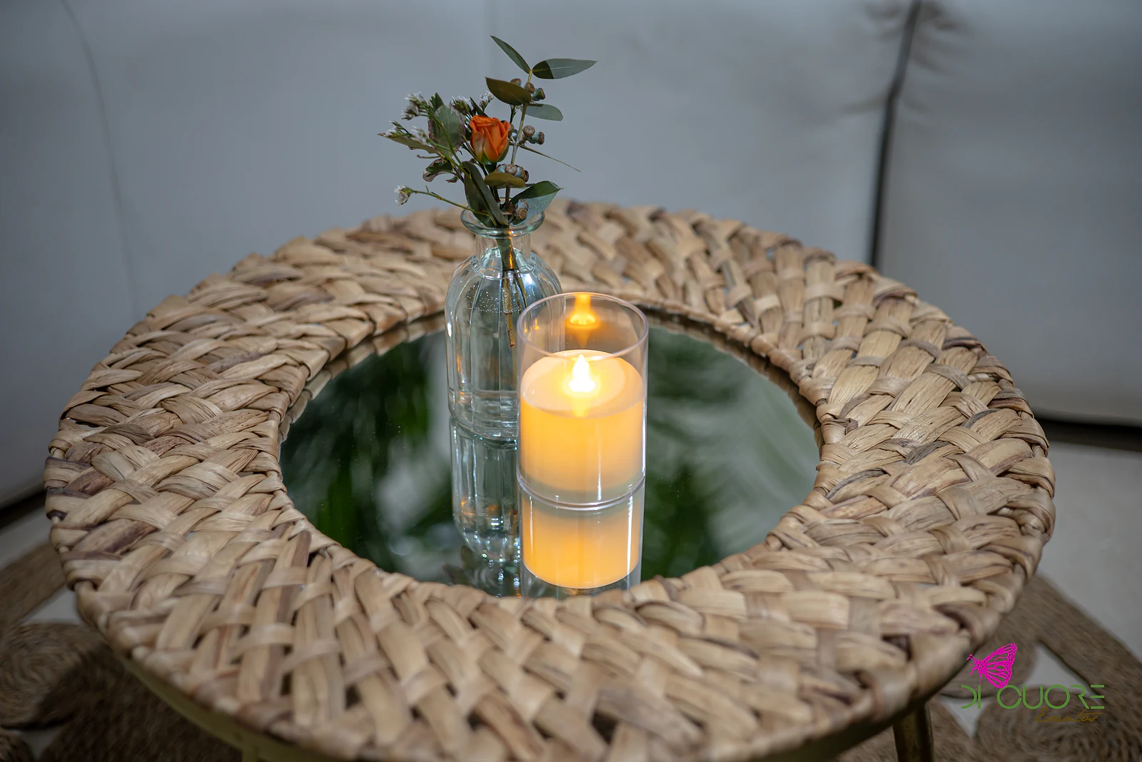 Mesa baixa de vime com tampo de espelho, jarro de vidro com uma flor cor de laranja e vela acesa