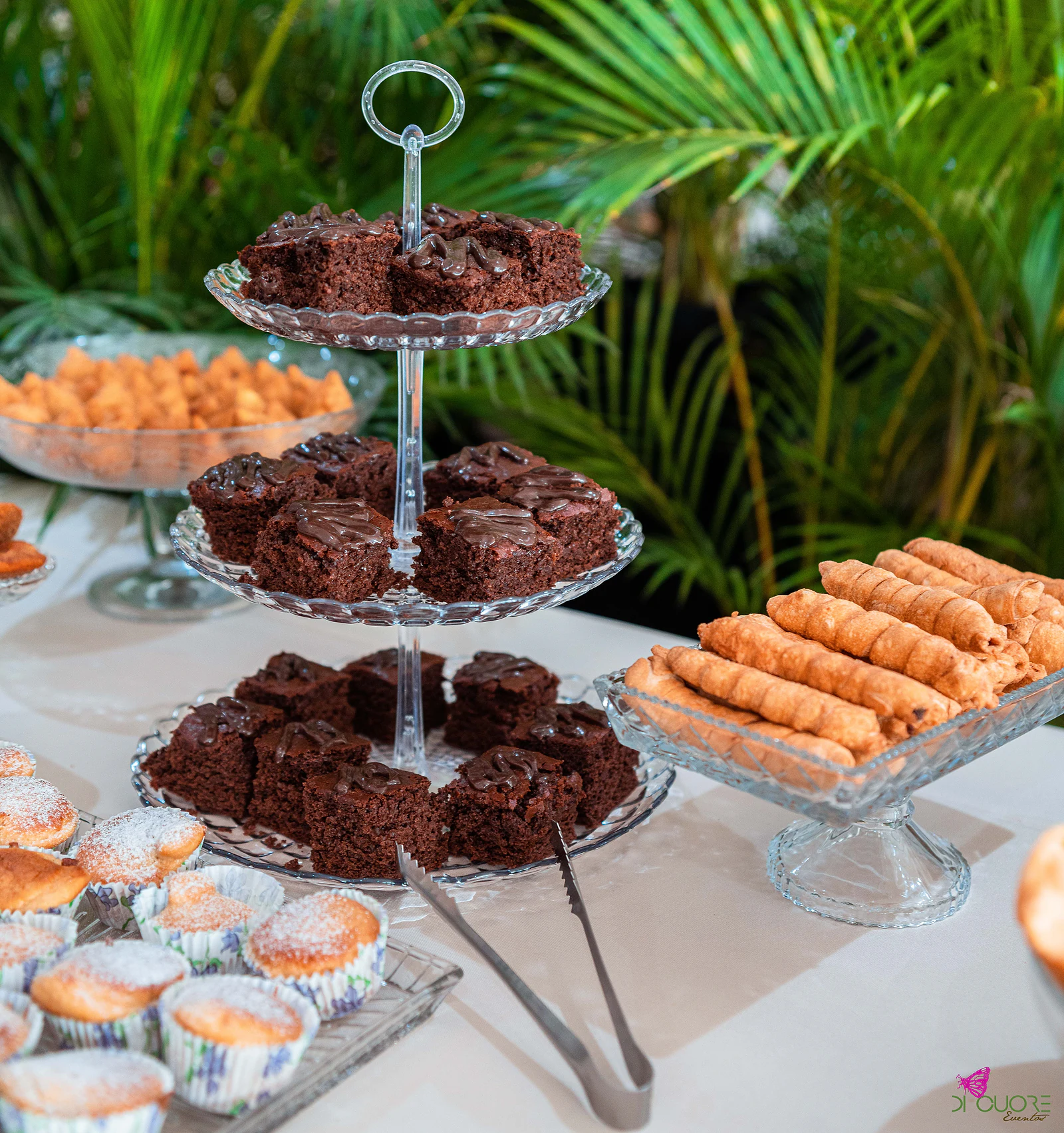 Brownies de chocolate em suporte de vidro de três andares, com palmeiras ao fundo