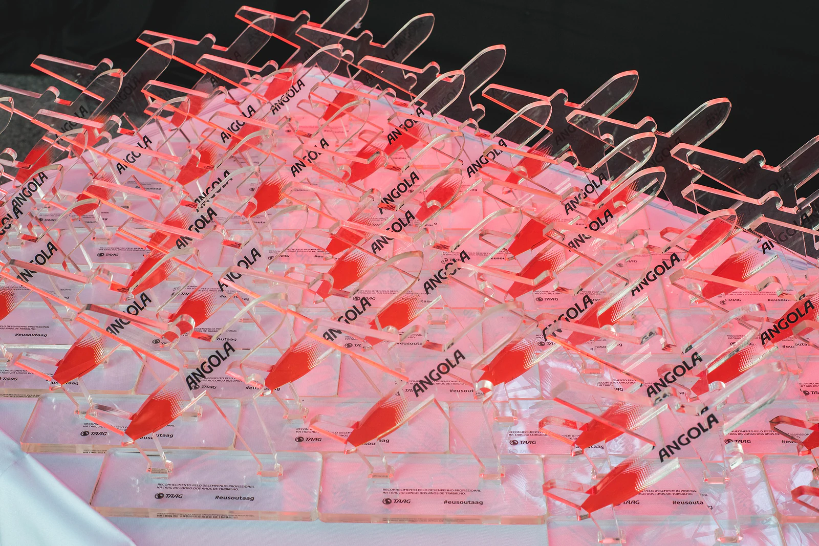 Rows of aeroplane-shaped acrylic awards engraved with the word Angola, in a red glow on a table