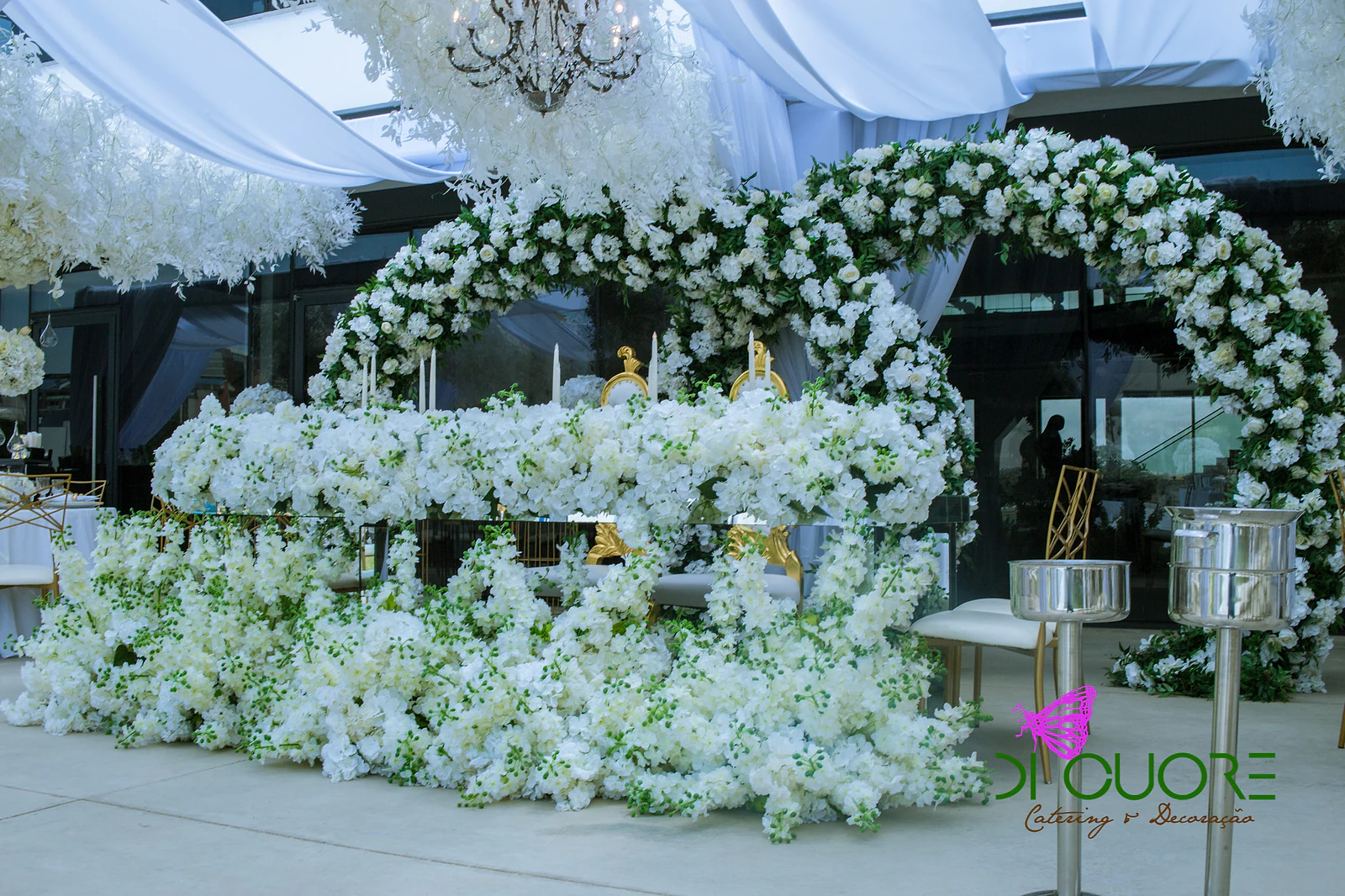Low table surrounded by white flowers, with an arch of white flowers behind and a crystal chandelier overhead