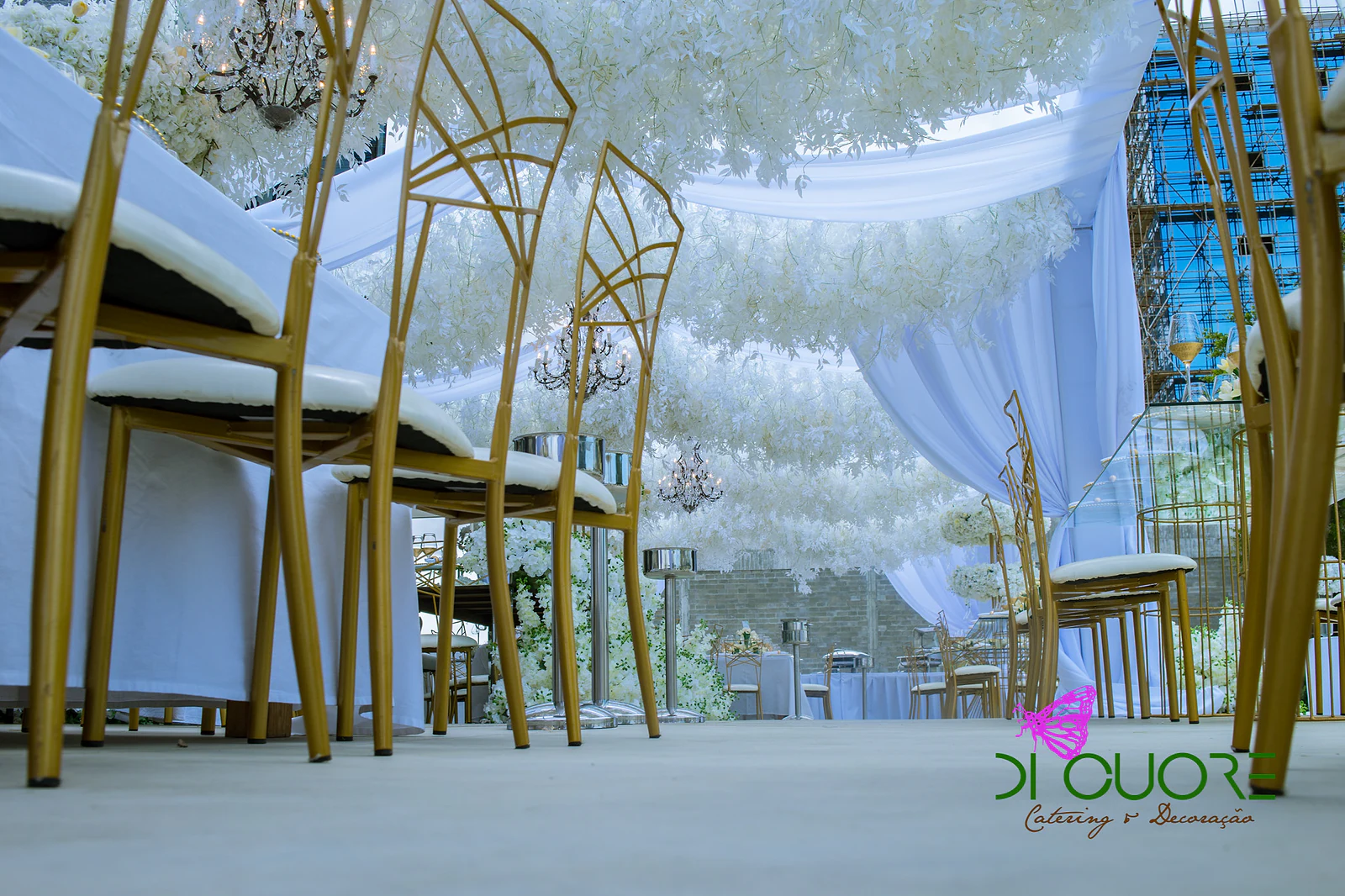 Golden open-backed chairs seen from below, beneath a ceiling of hanging white flowers and light drapes