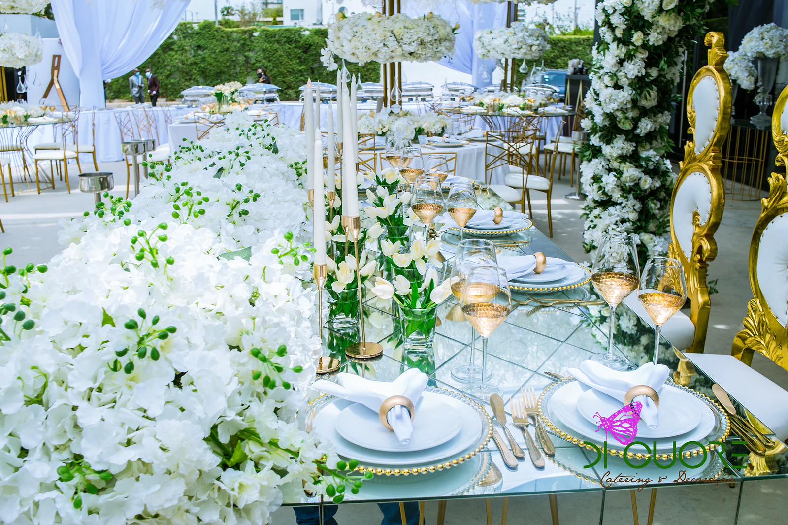 Mirror-topped table with a band of white hydrangeas, tulips, candles and plates with gold rings, beside a white and gold armchair