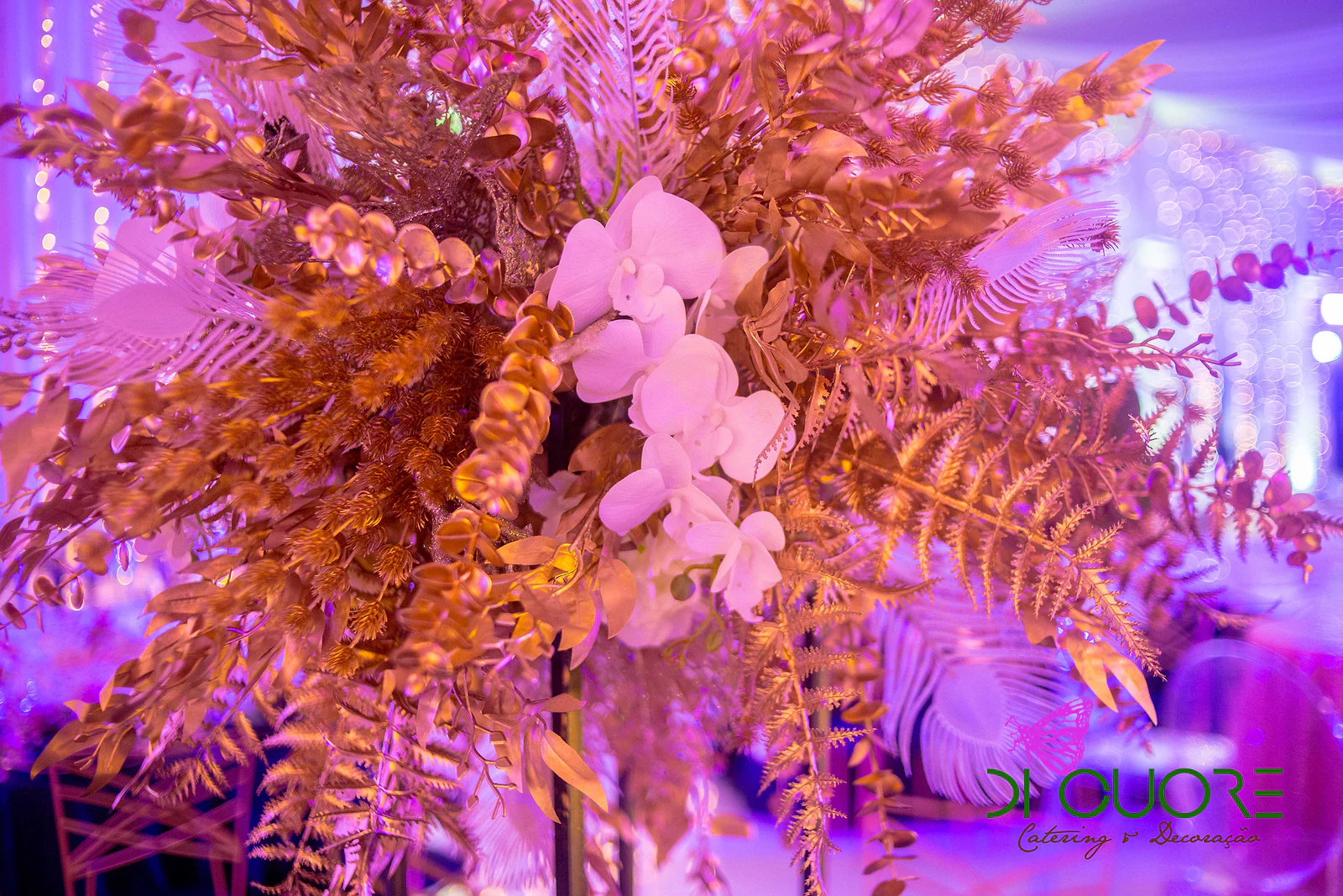 Pormenor de um centro de mesa de folhas e fetos dourados com orquídeas brancas