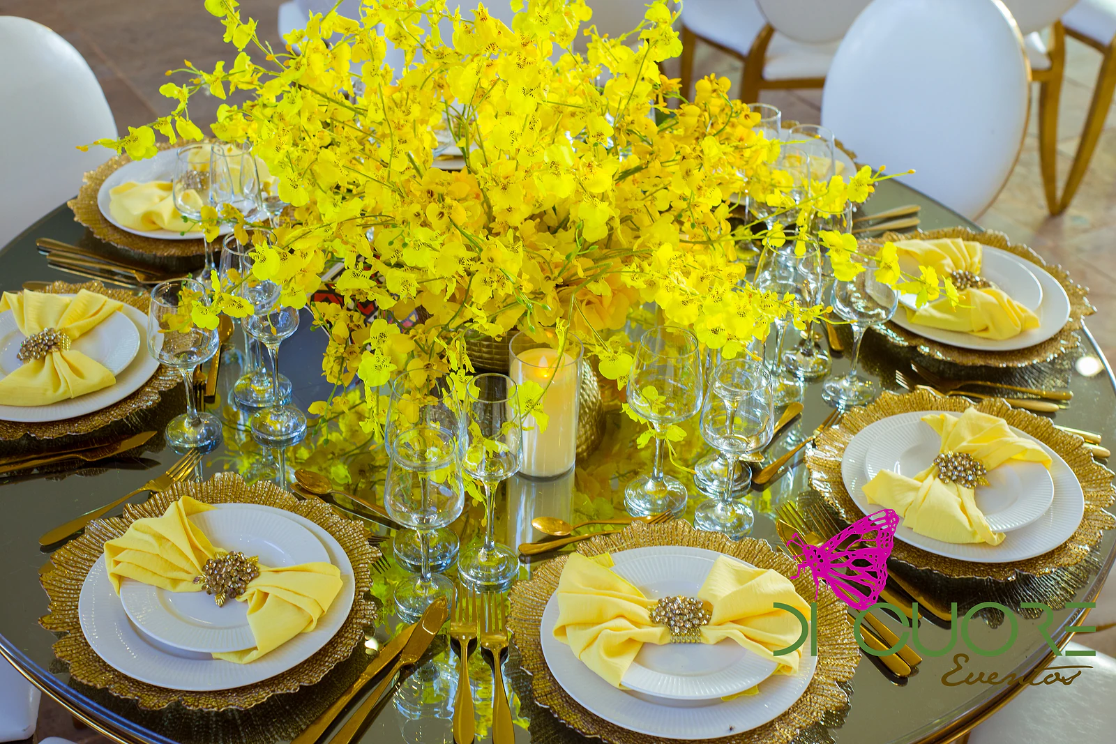 Round mirror-topped table seen from above, with place settings of pale yellow napkins and a large centrepiece of yellow orchids