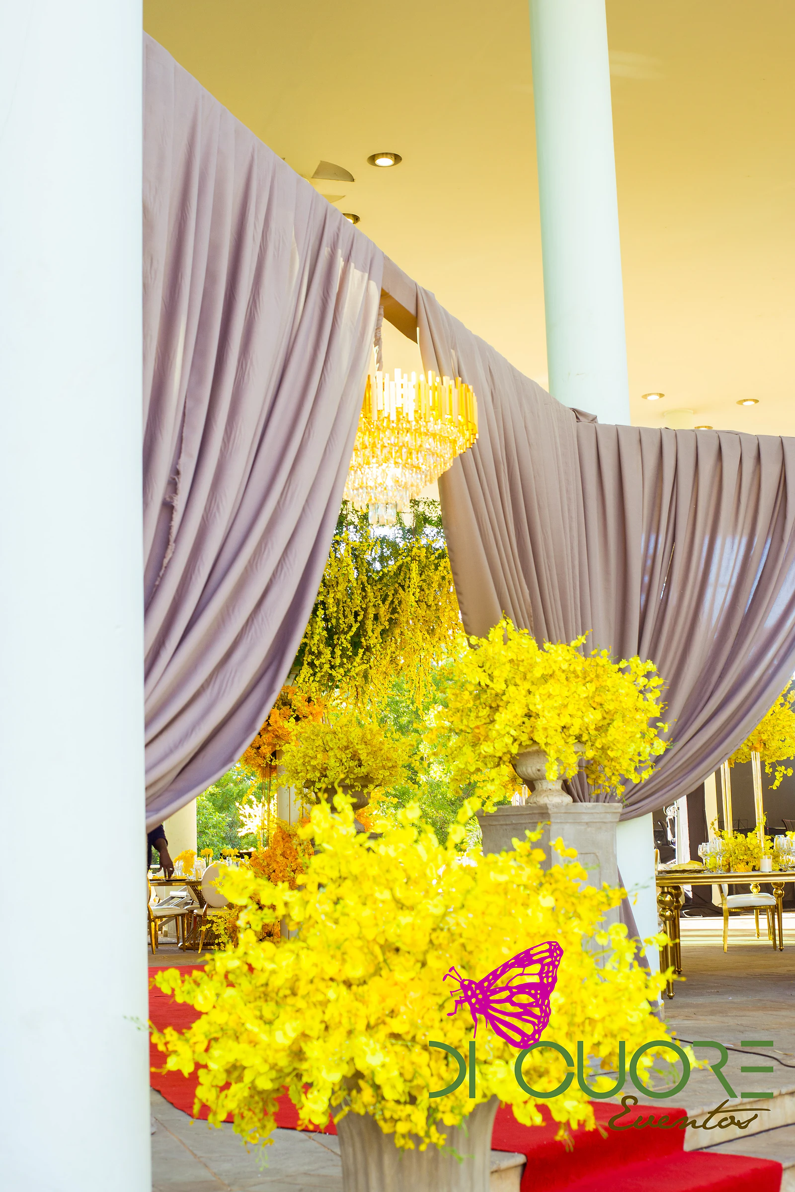 Pleated dusty-pink drapes over the entrance, with a large spray of yellow orchids in a stone urn and the red carpet