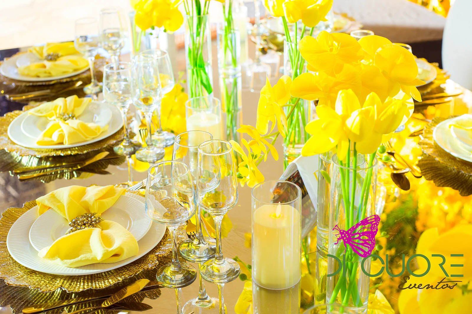 Table with yellow tulips in glass vases, candles and pale yellow napkins on gold chargers