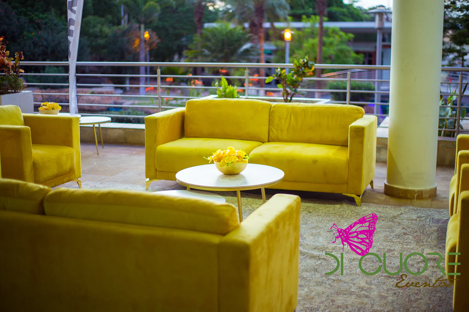 Terrace with yellow sofas around a low white table holding a bowl of yellow flowers, beside a white column