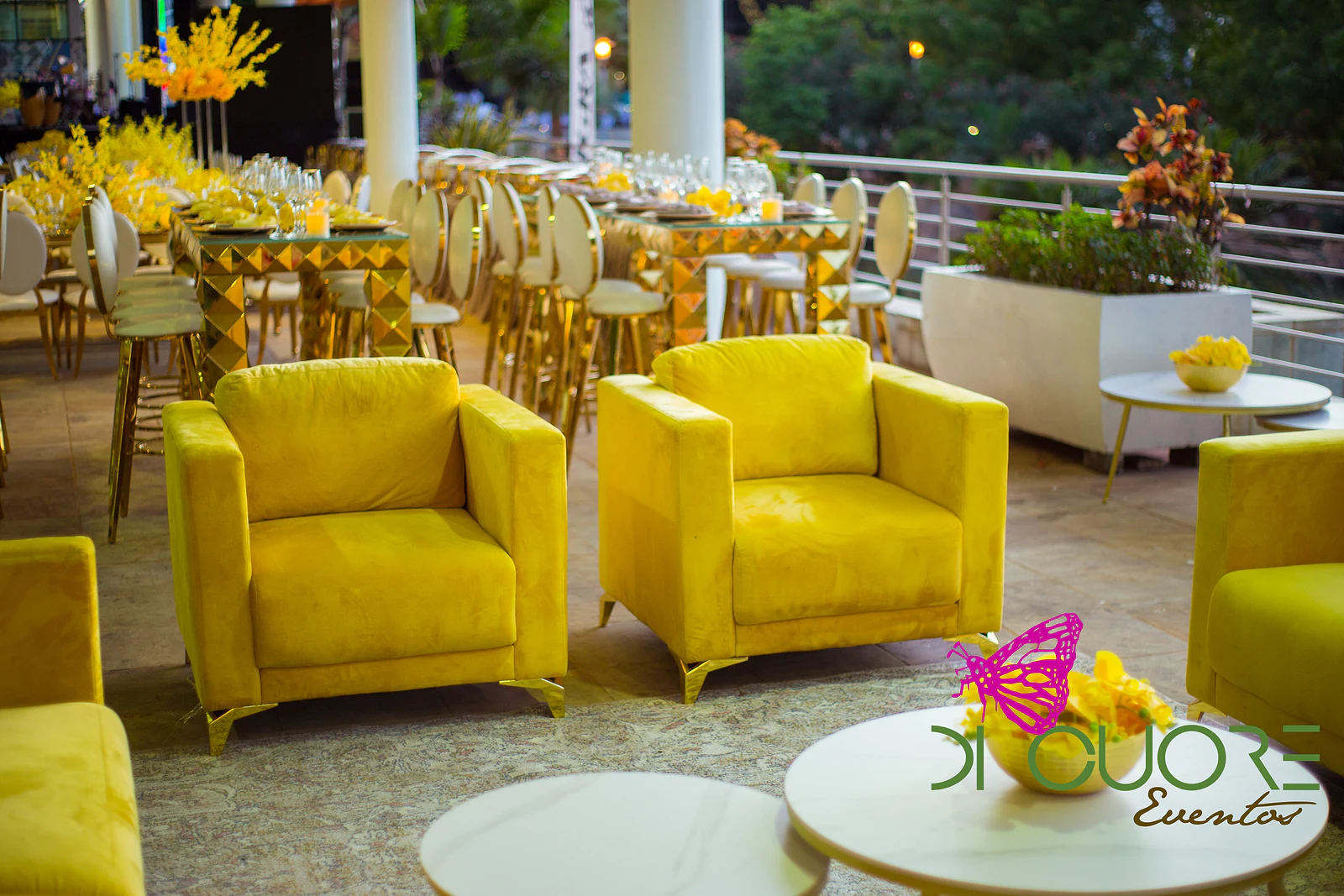 Yellow armchairs and low white tables on the terrace, with gold pyramid tables and tall stools behind