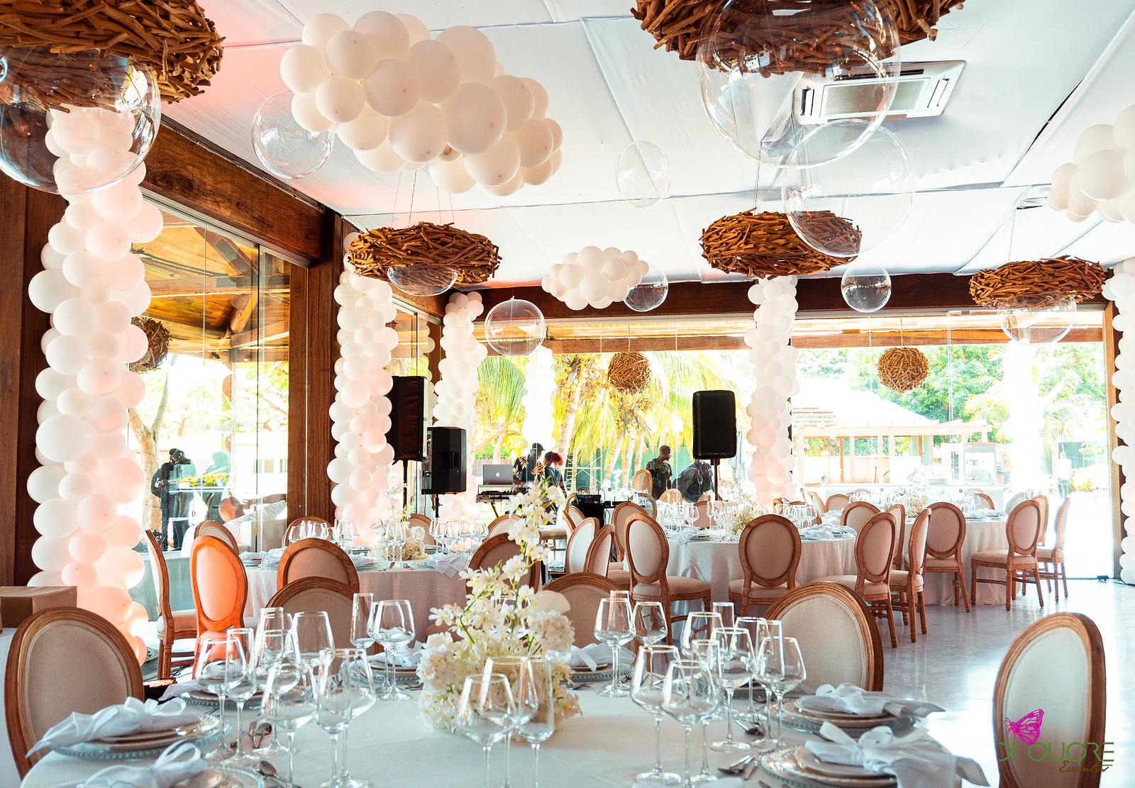 Hall with round tables and medallion-back chairs, balloon columns and clouds, and twig nests hanging from the ceiling