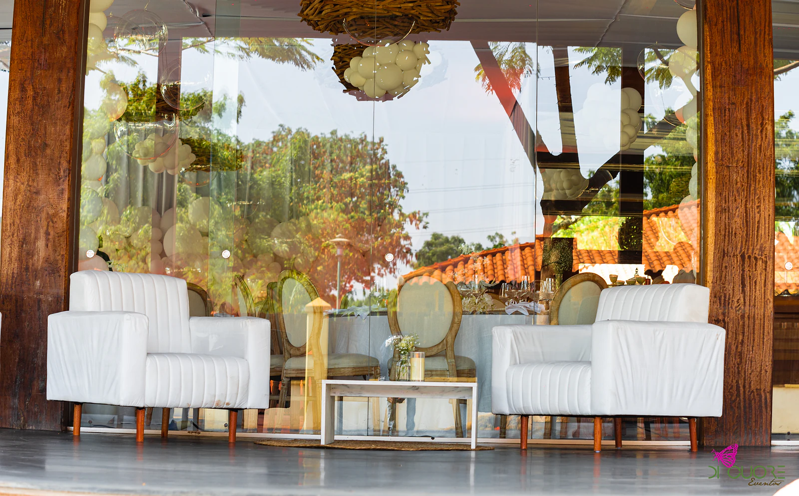 White armchairs and a coffee table beside a glass wall overlooking the garden