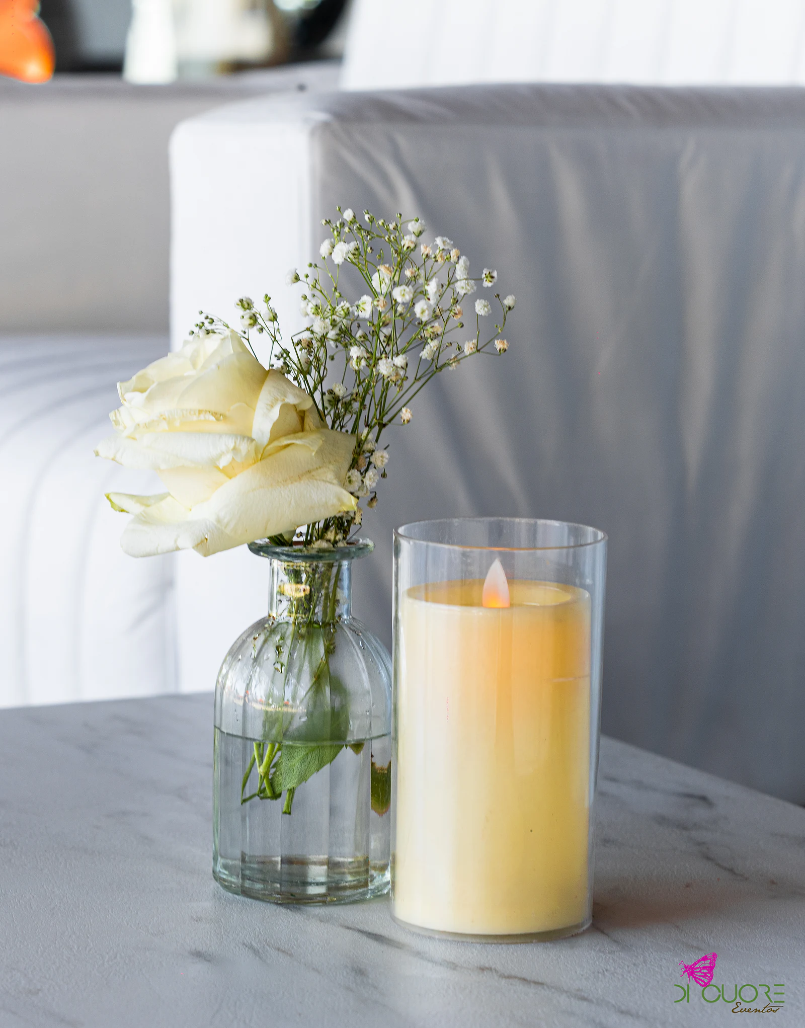 White rose and gypsophila in a glass bottle beside a candle in a glass holder, on a marble table