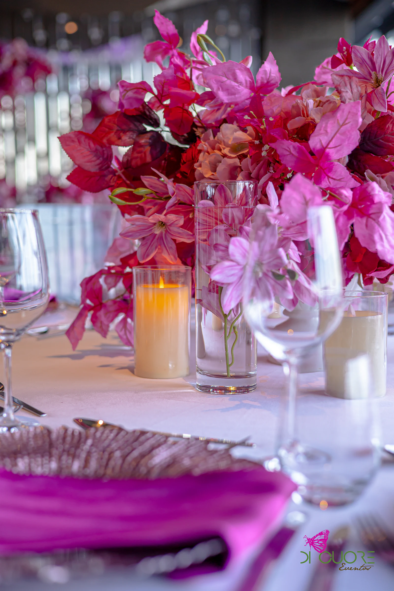 Arrangement of fuchsia and pink flowers with a candle and glasses, and a fuchsia satin napkin on a rose-copper charger